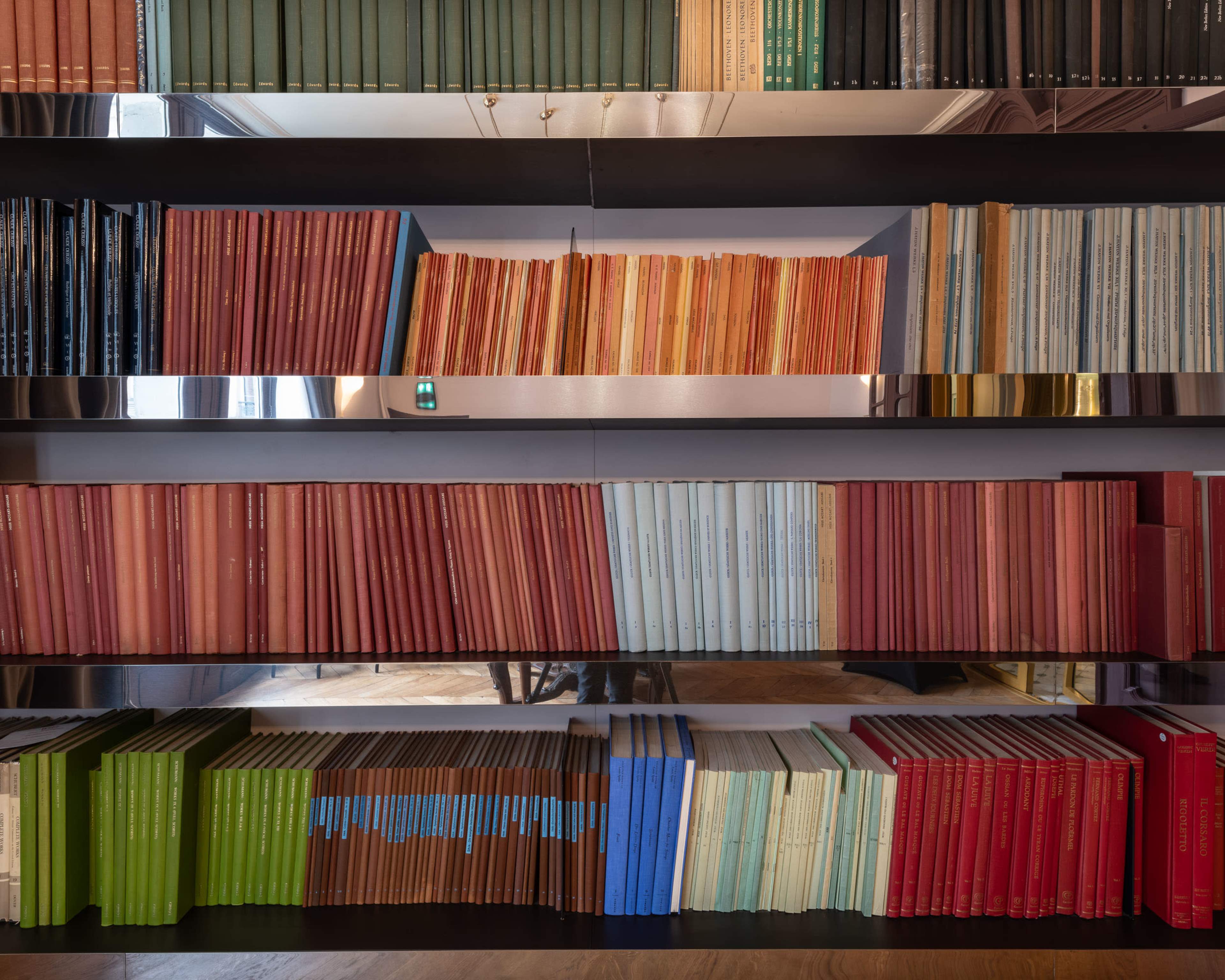 A bookshelf displays neatly arranged books in various colors, including red, green, blue, and beige, on multiple shelves.