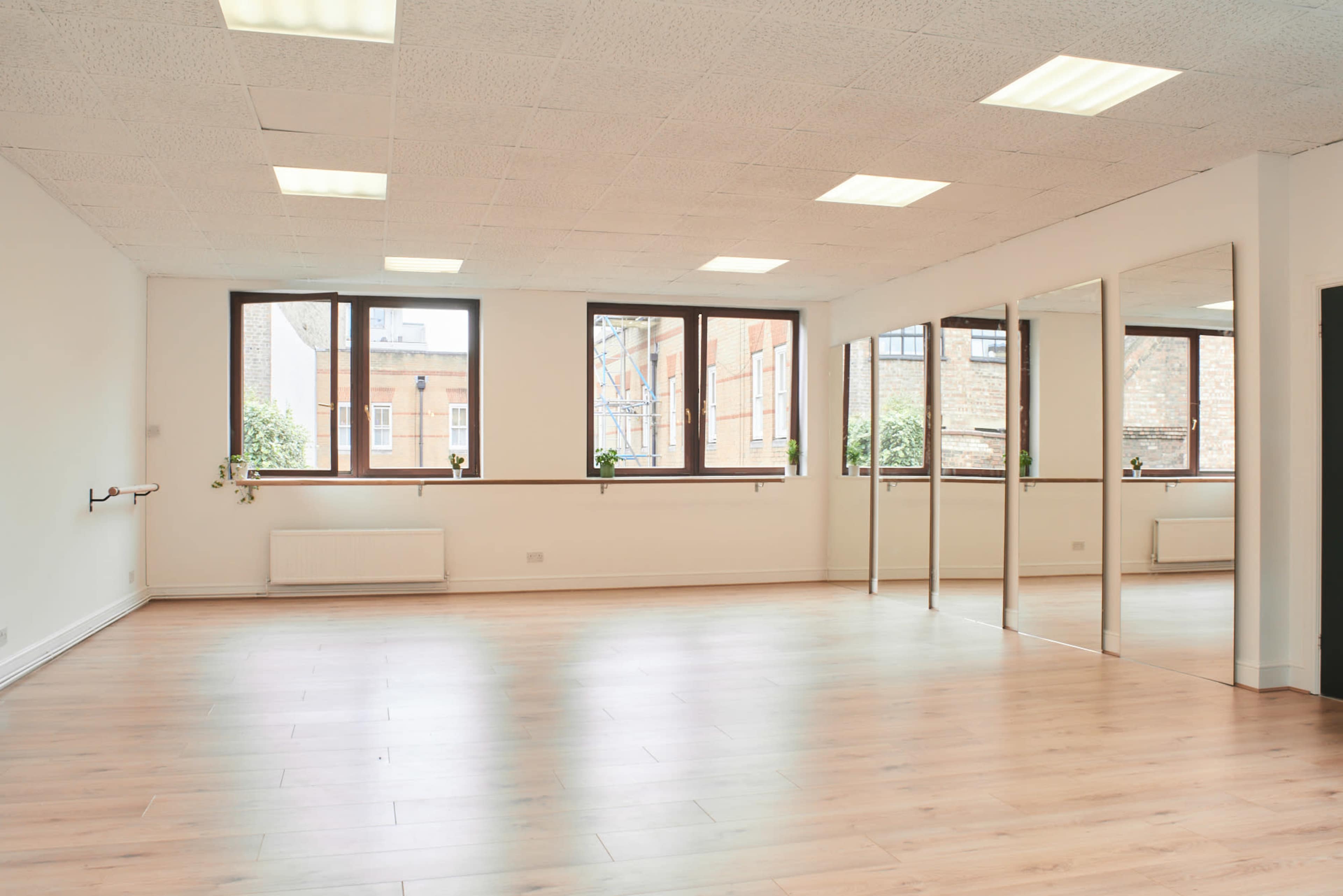 A spacious, well-lit room with large windows, hardwood flooring, and a wall of mirrors.