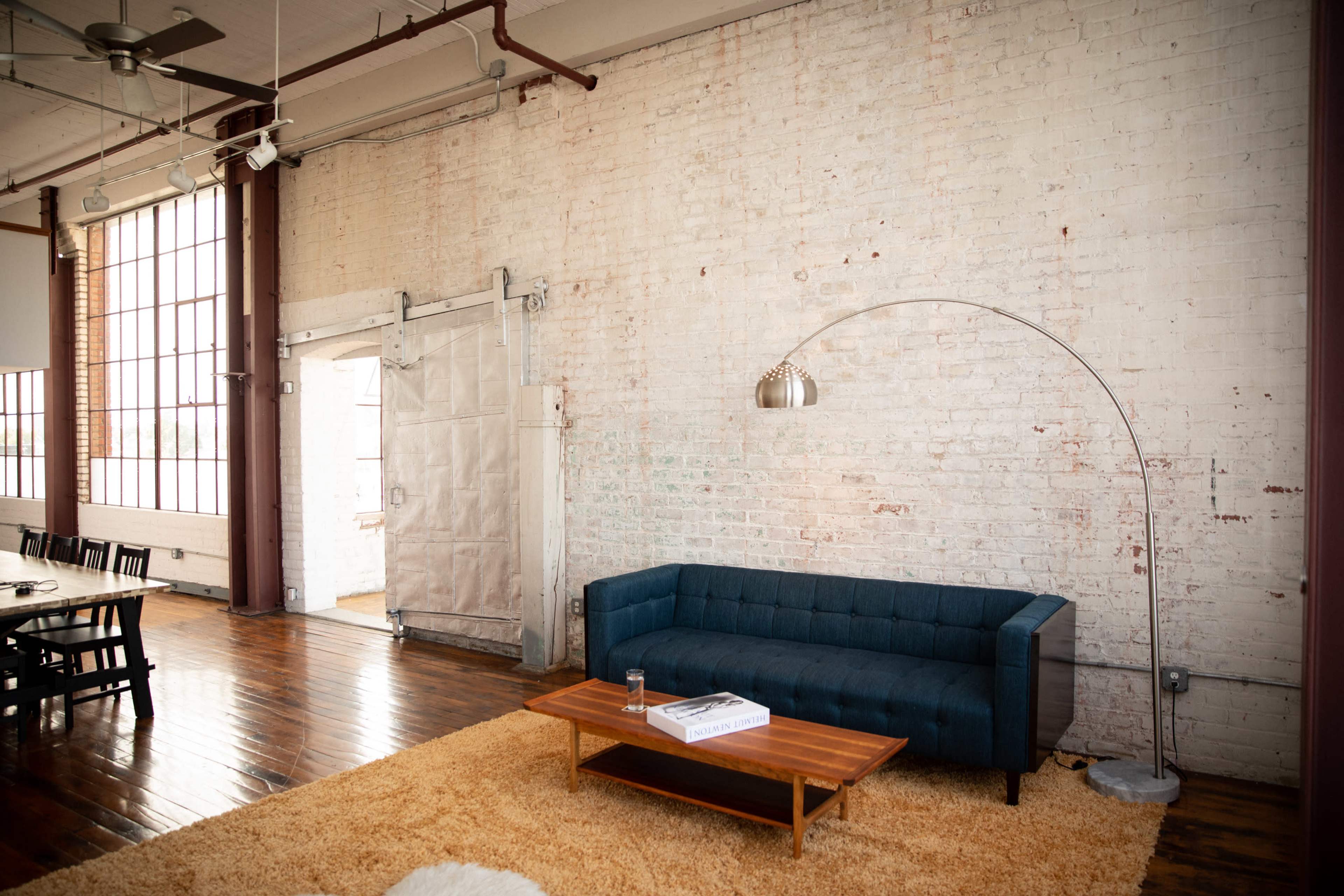 A spacious living area featuring a blue couch, a wooden coffee table, an arc floor lamp, and a large window with an industrial-style door.