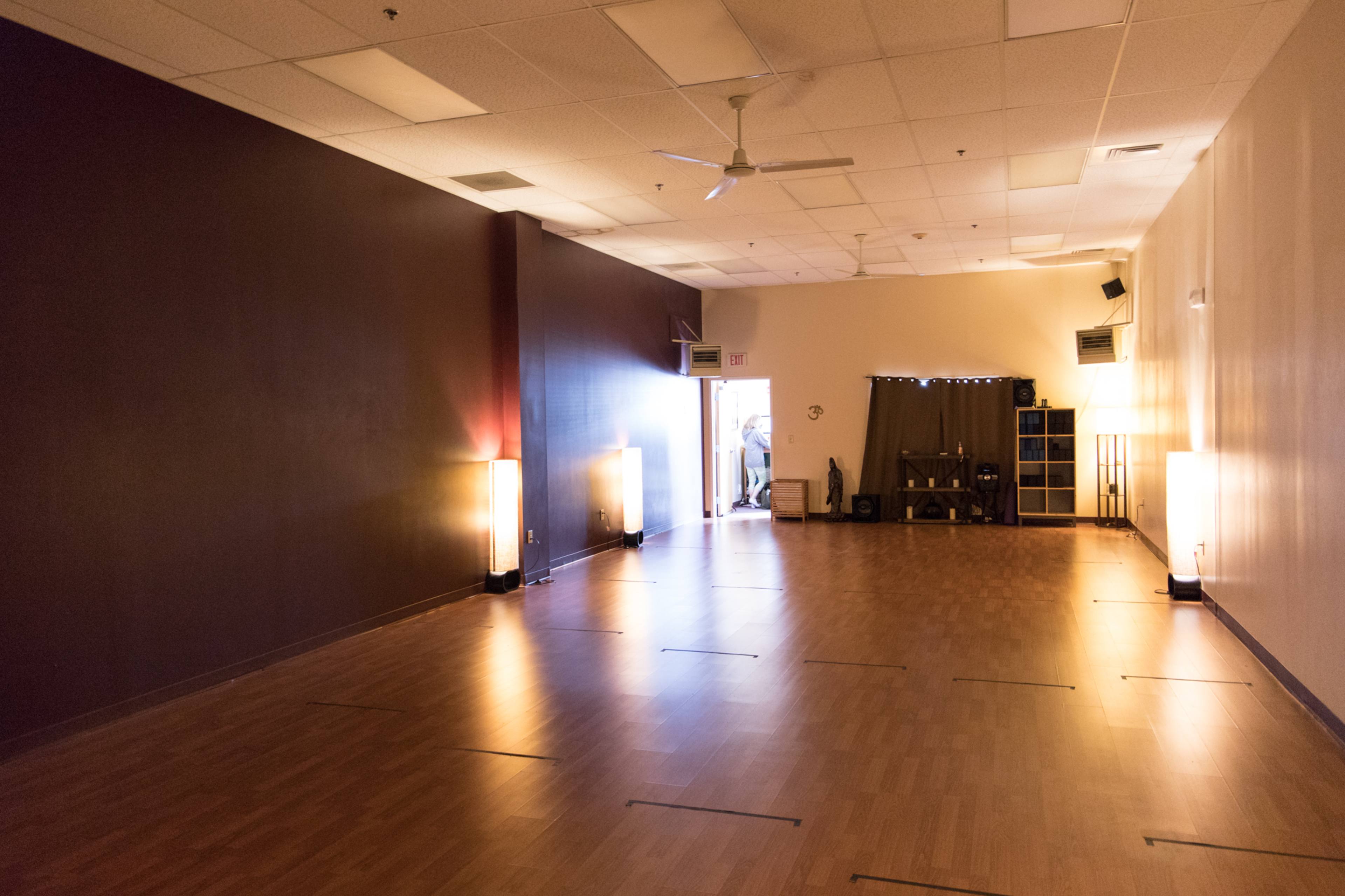 A spacious, empty indoor room with wooden flooring and soft lighting, featuring a doorway at one end.