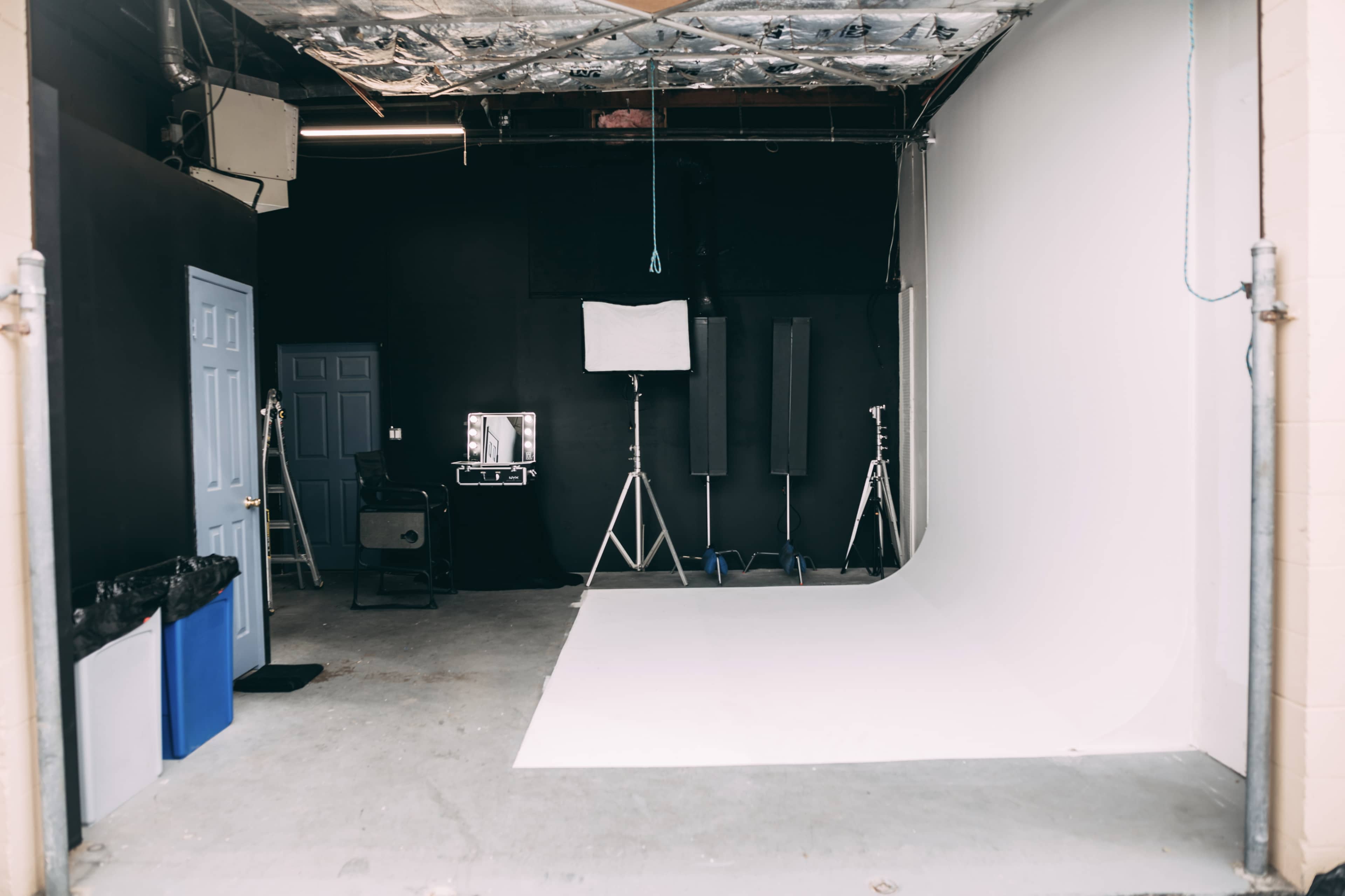 A photography studio with a white backdrop, lighting equipment, and various props arranged in a corner.