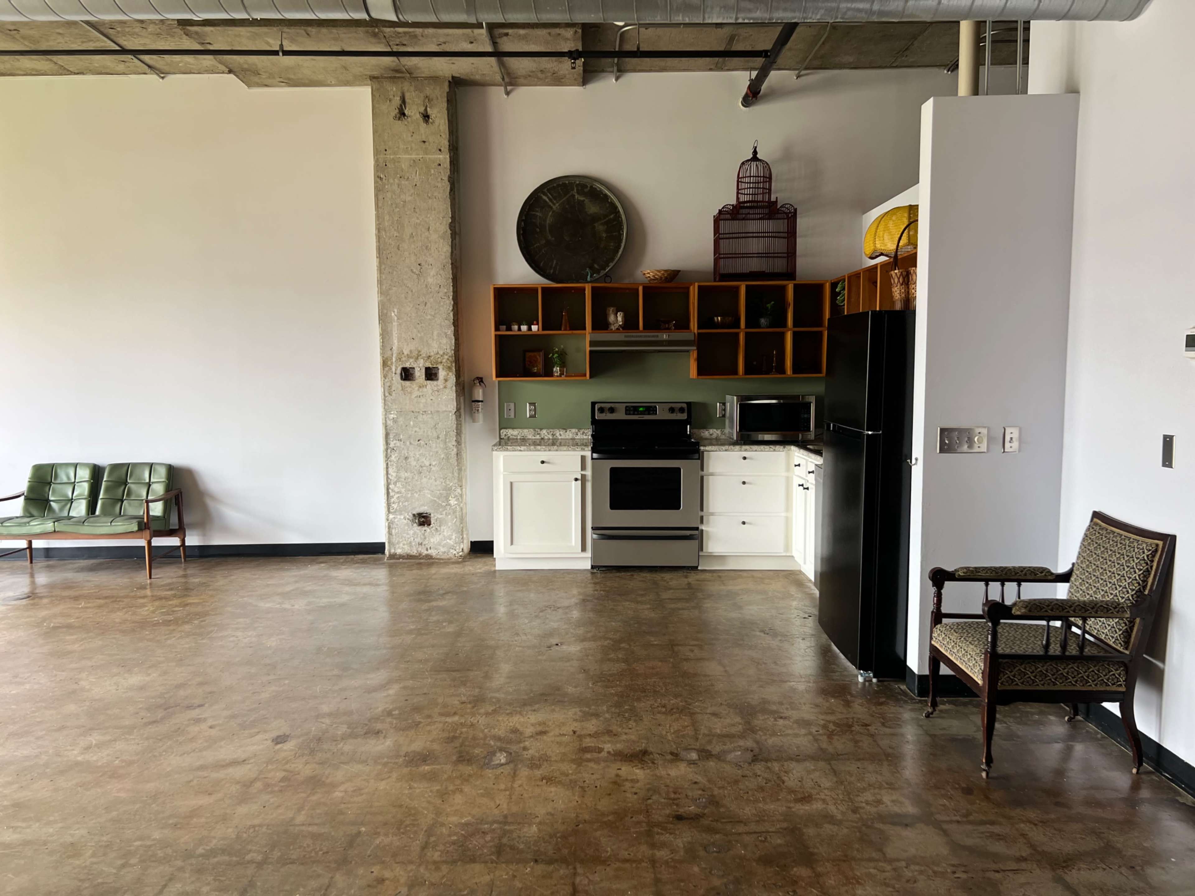 An open kitchen area with a stove, refrigerator, and shelves, accompanied by a small dining table and two seating areas.