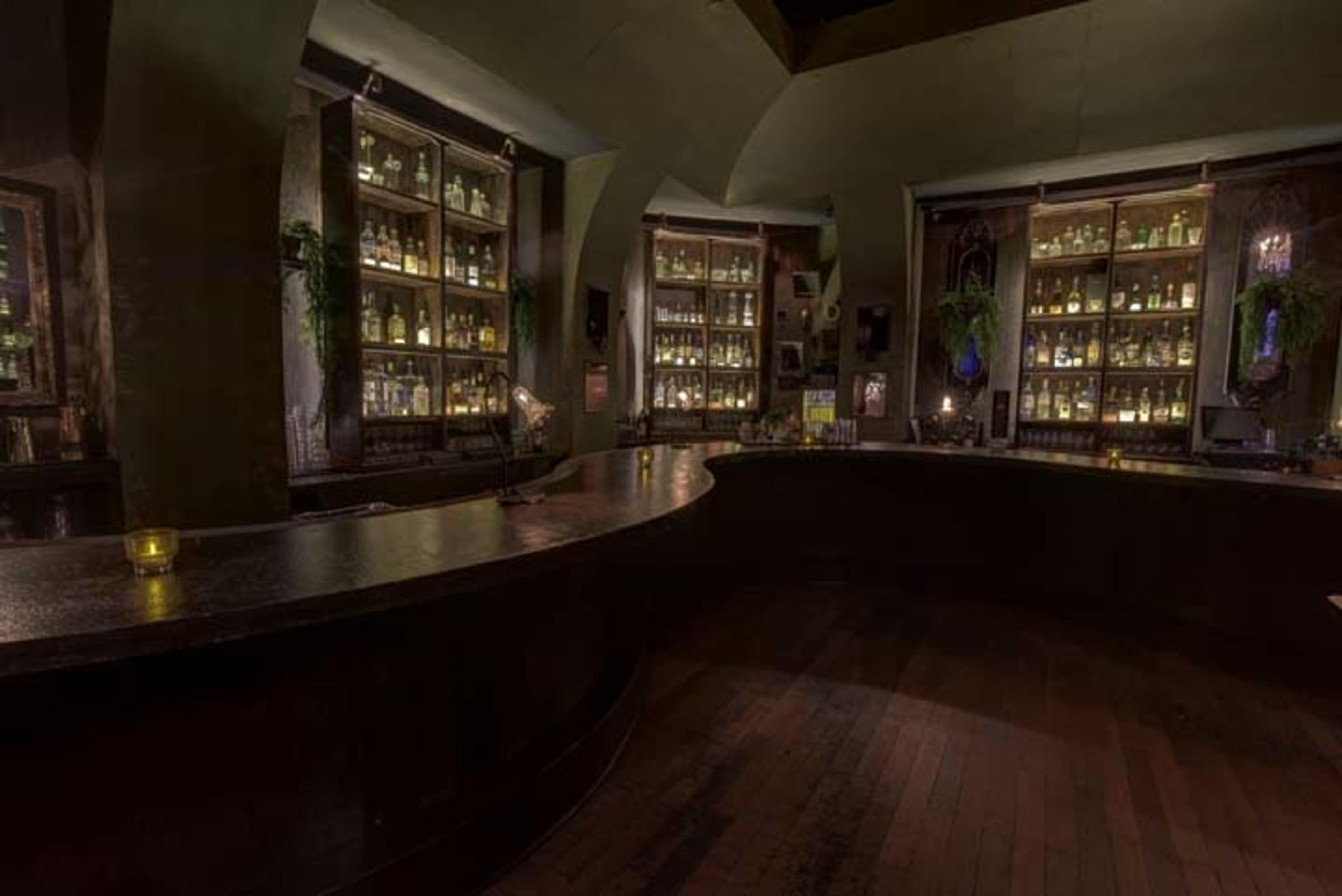 A dimly lit bar with shelves of glass bottles displayed behind a curved wooden counter.