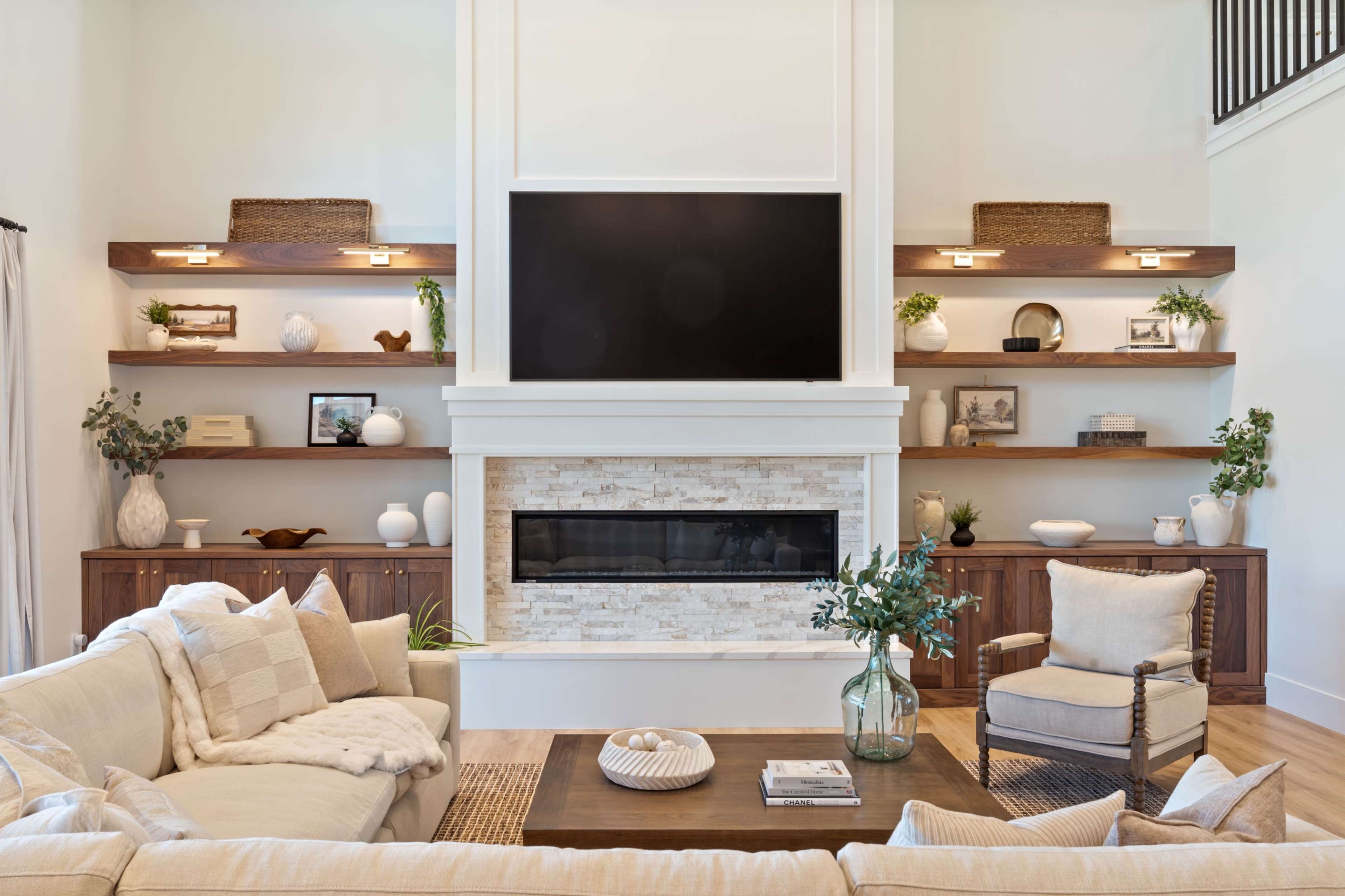 The image shows a modern living room featuring a large flat-screen television mounted above a fireplace, surrounded by wooden shelves displaying decorative items.