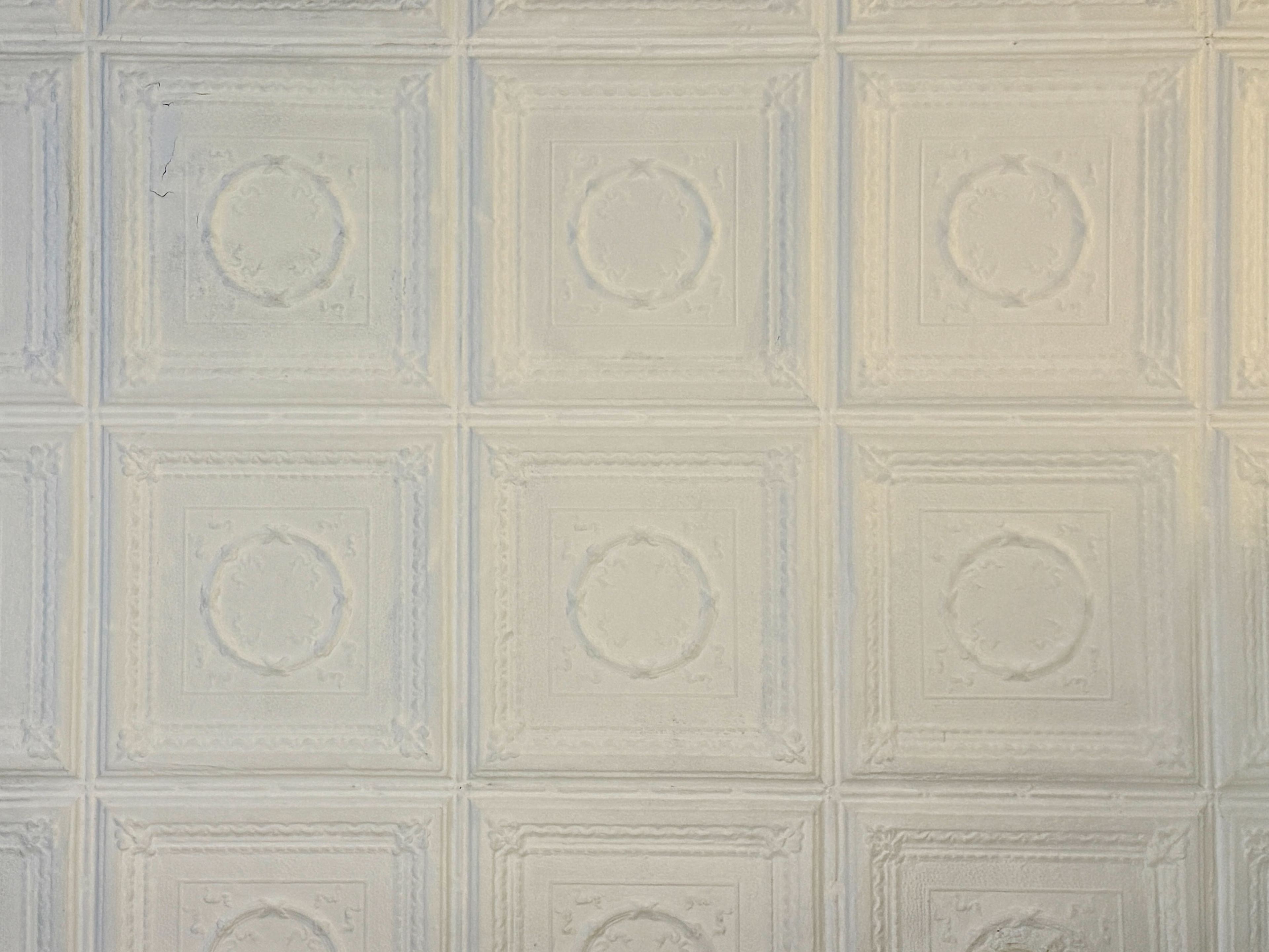 The image shows a textured wall featuring a repeated pattern of square panels with circular designs.