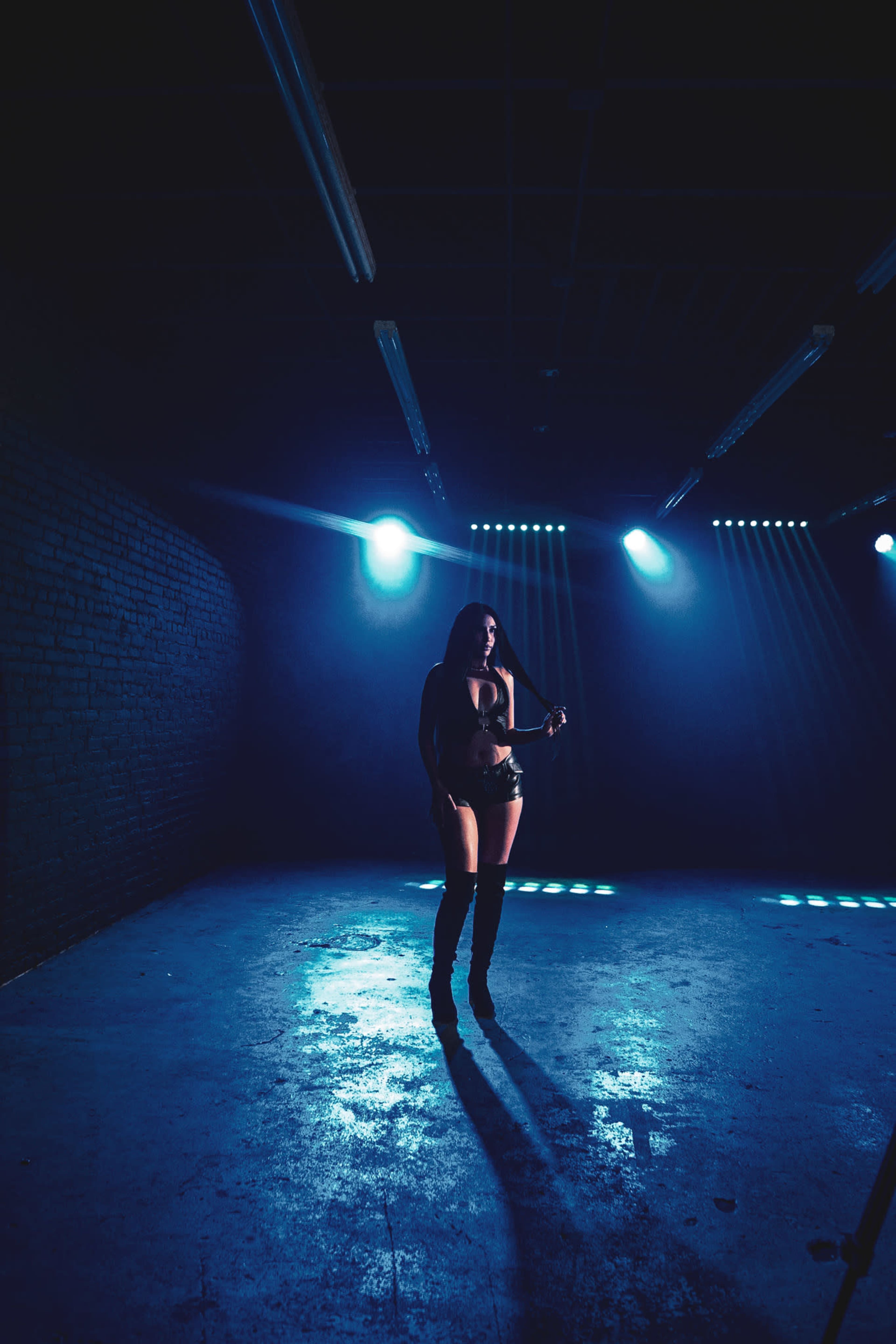 A figure stands under dramatic lighting in an empty, dimly lit space with textured walls.