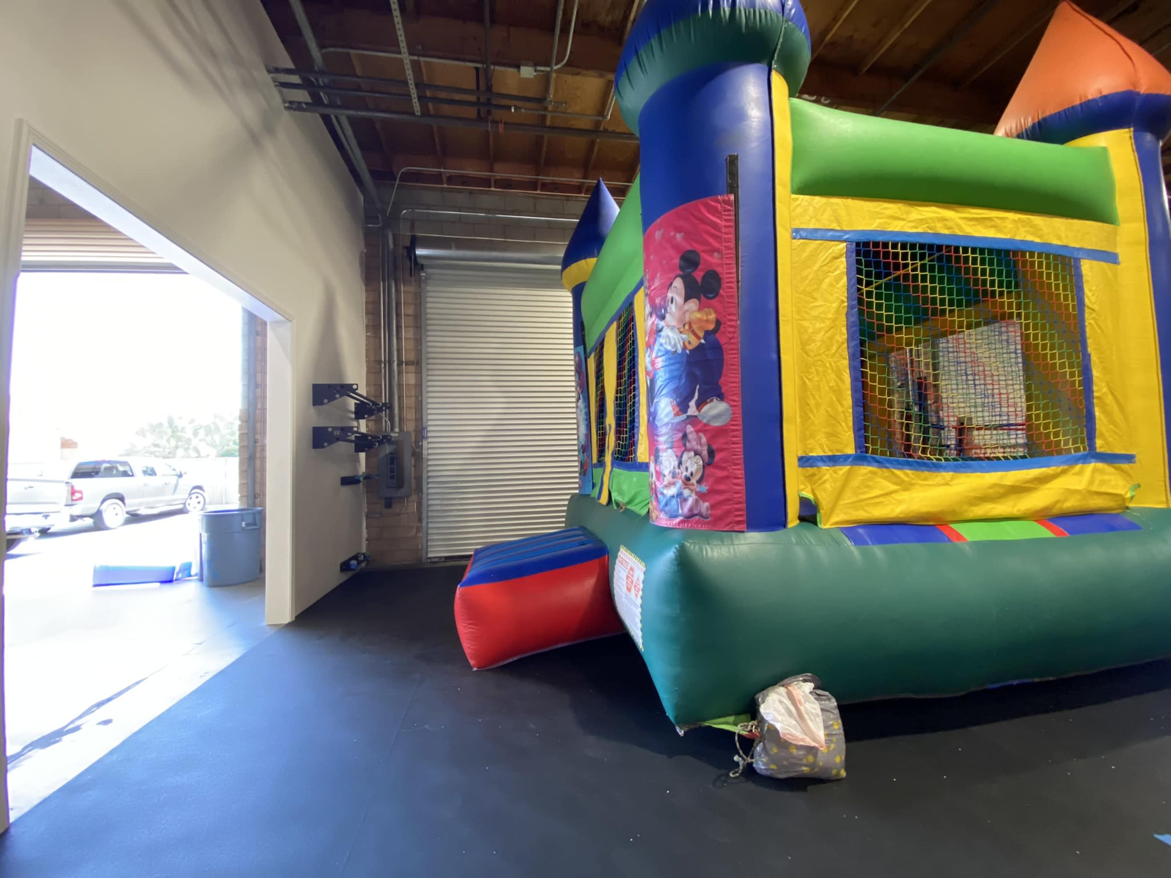 A brightly colored inflatable bounce house set up indoors near an open door, with a view of a parking lot outside.