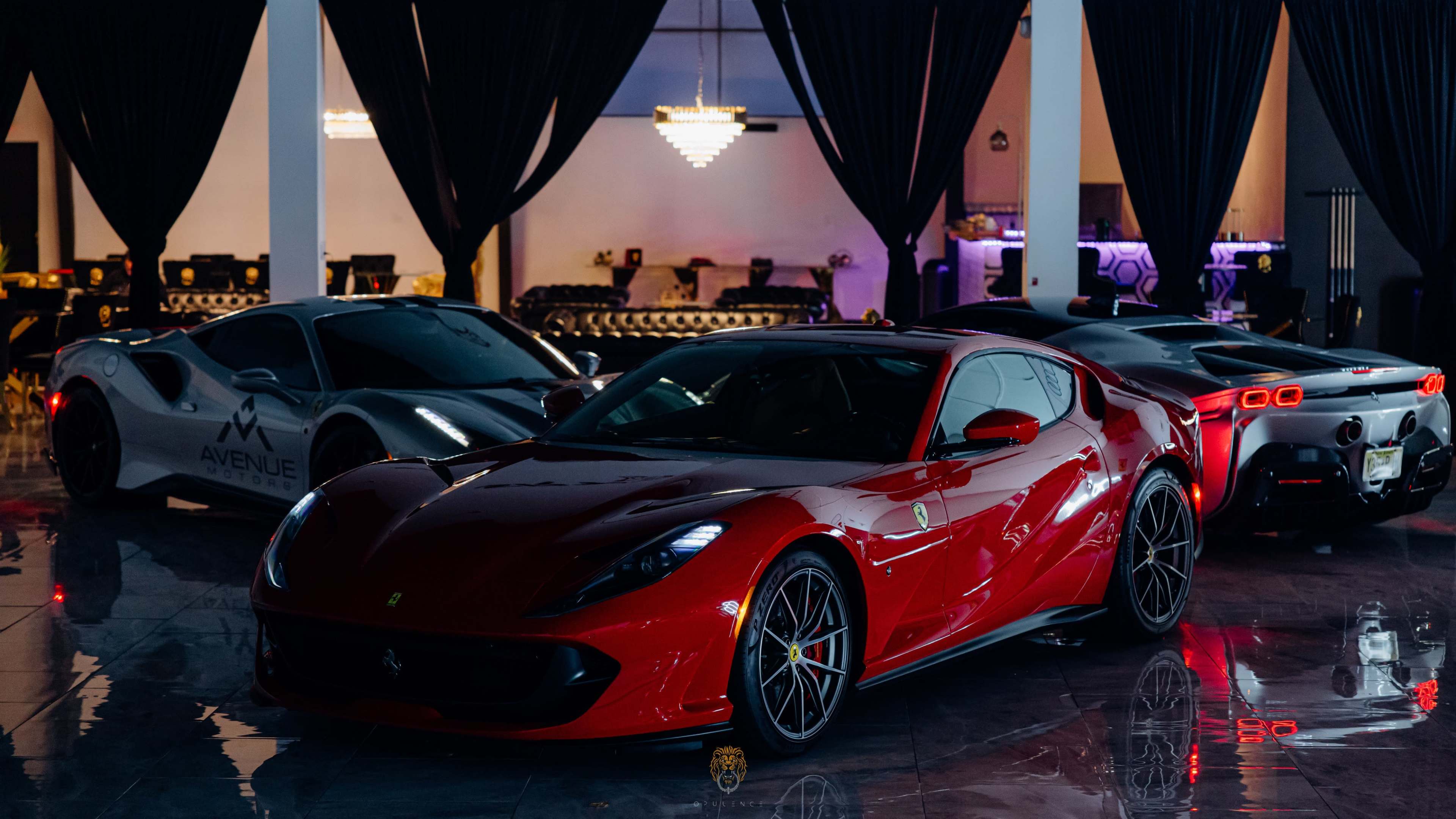 The image features a sleek red Ferrari parked in front of two other luxury cars, one silver and another black, in a well-lit automotive showroom.