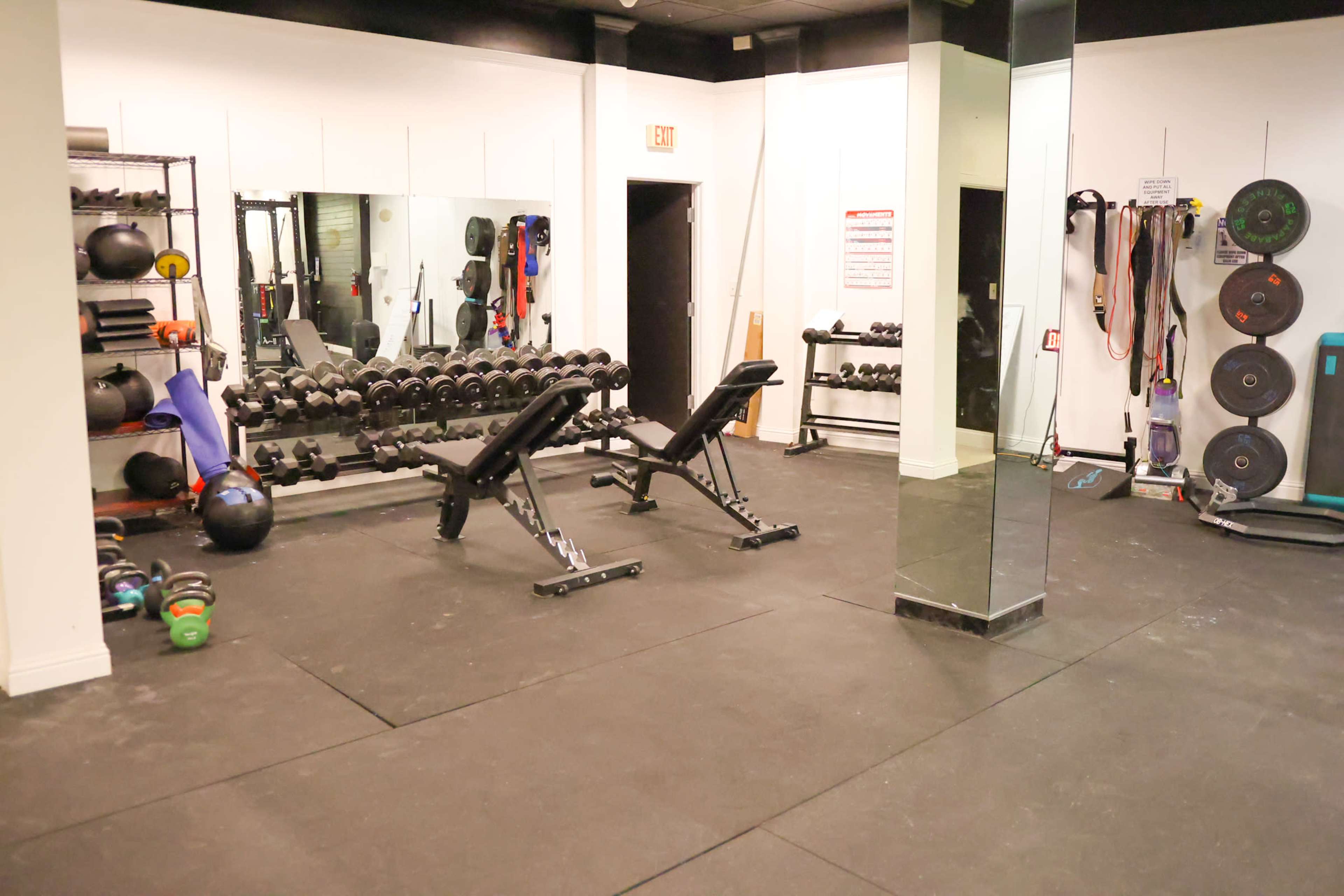 A fitness room with various weights, benches, and exercise equipment arranged around mirrors and walls.