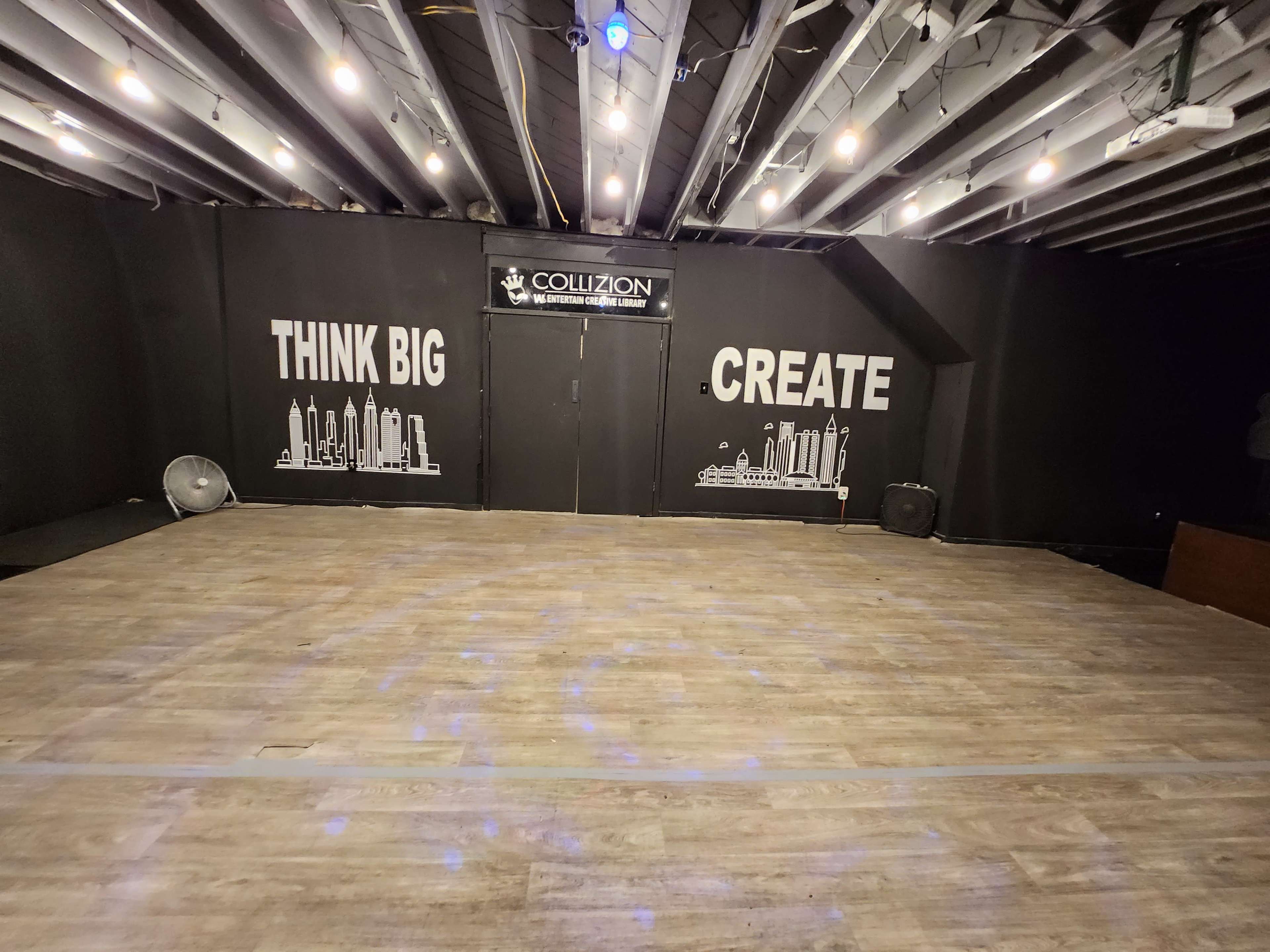A spacious indoor area with a wooden floor and a black wall featuring the phrases "THINK BIG" and "CREATE" alongside city skyline graphics.