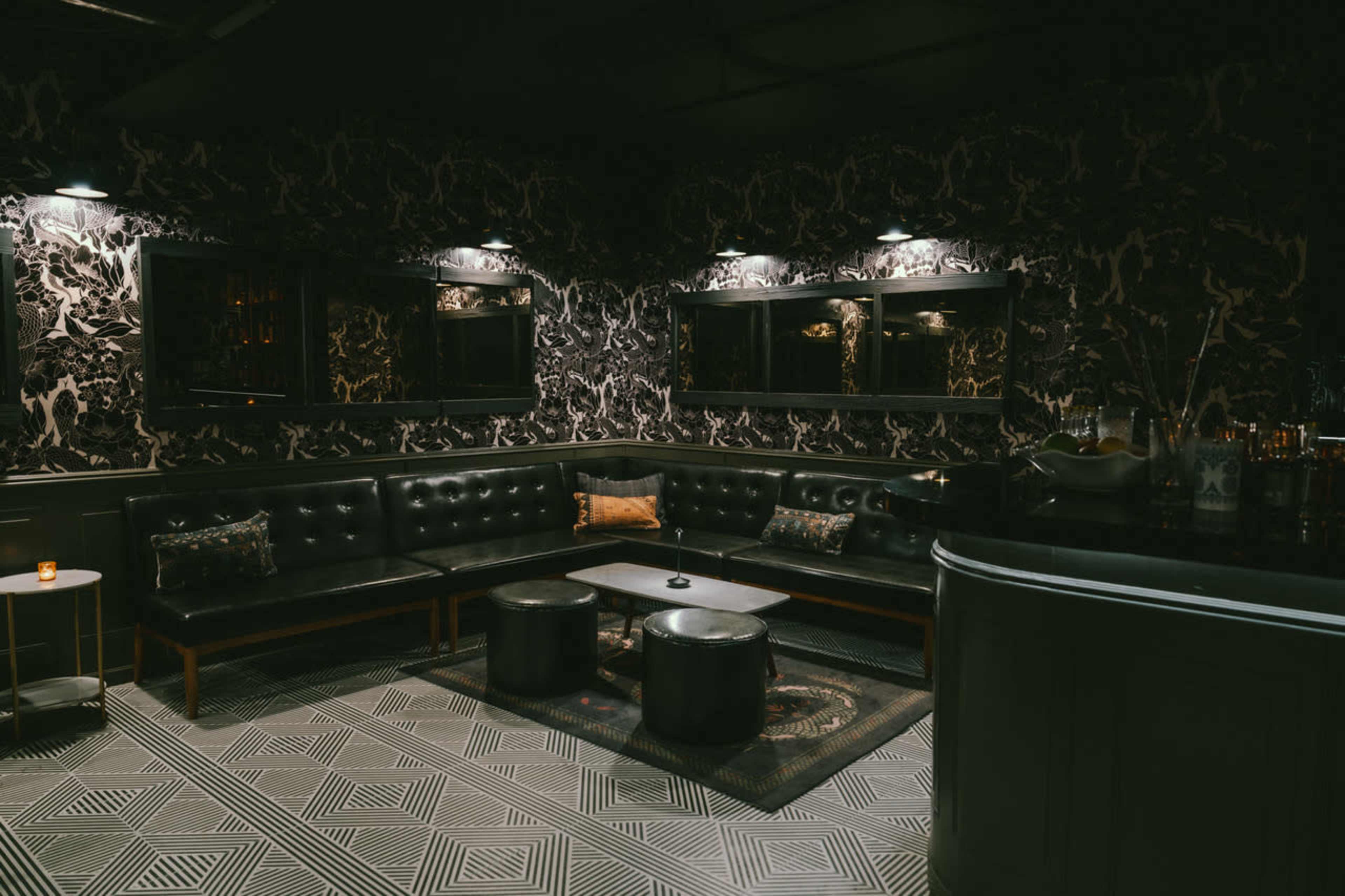 The image shows a dimly lit lounge area with black leather seating, patterned walls, and a geometric tiled floor.
