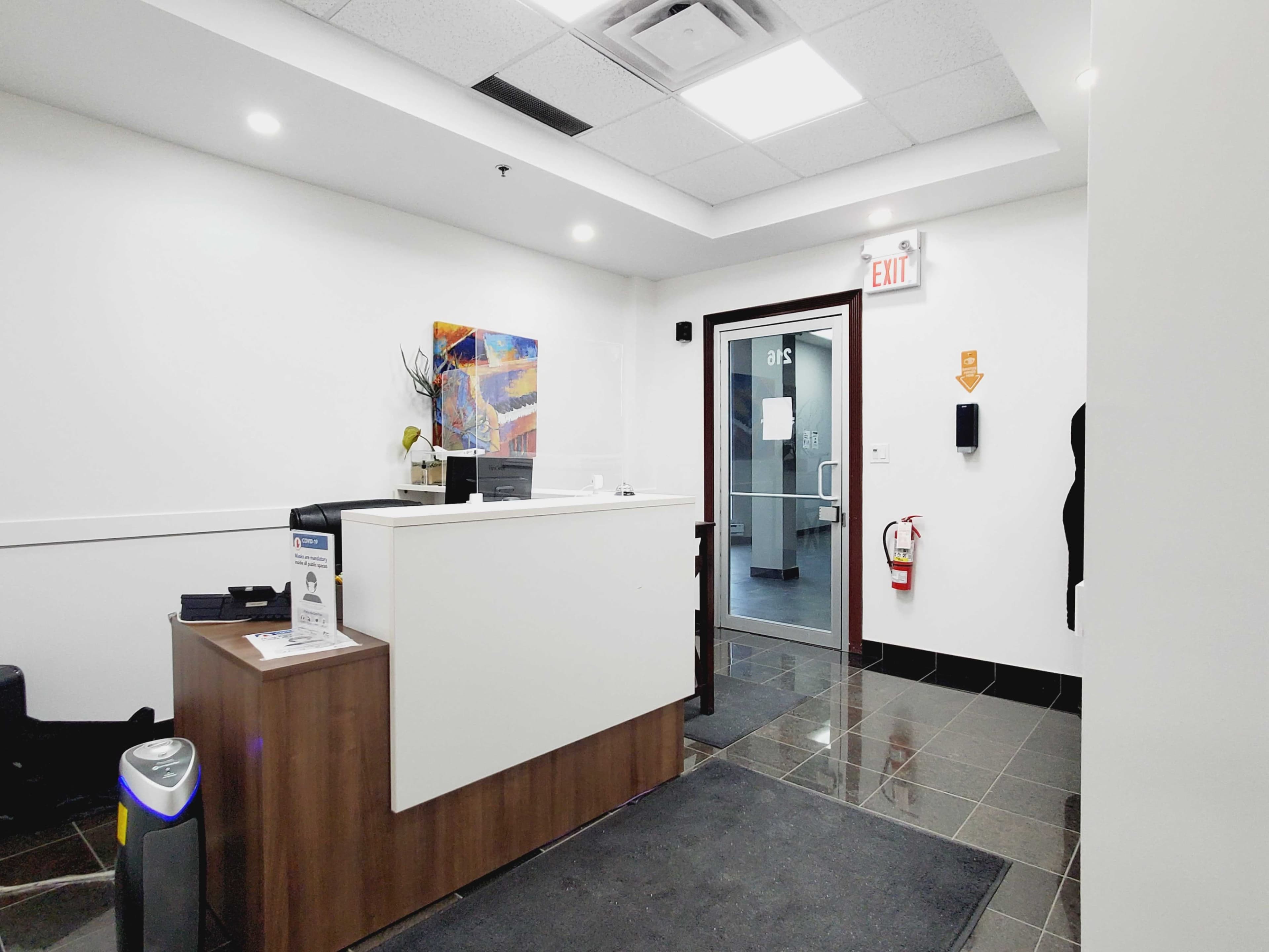 The interior of a modern reception area with a countertop, chairs, and a glass door leading to another room.