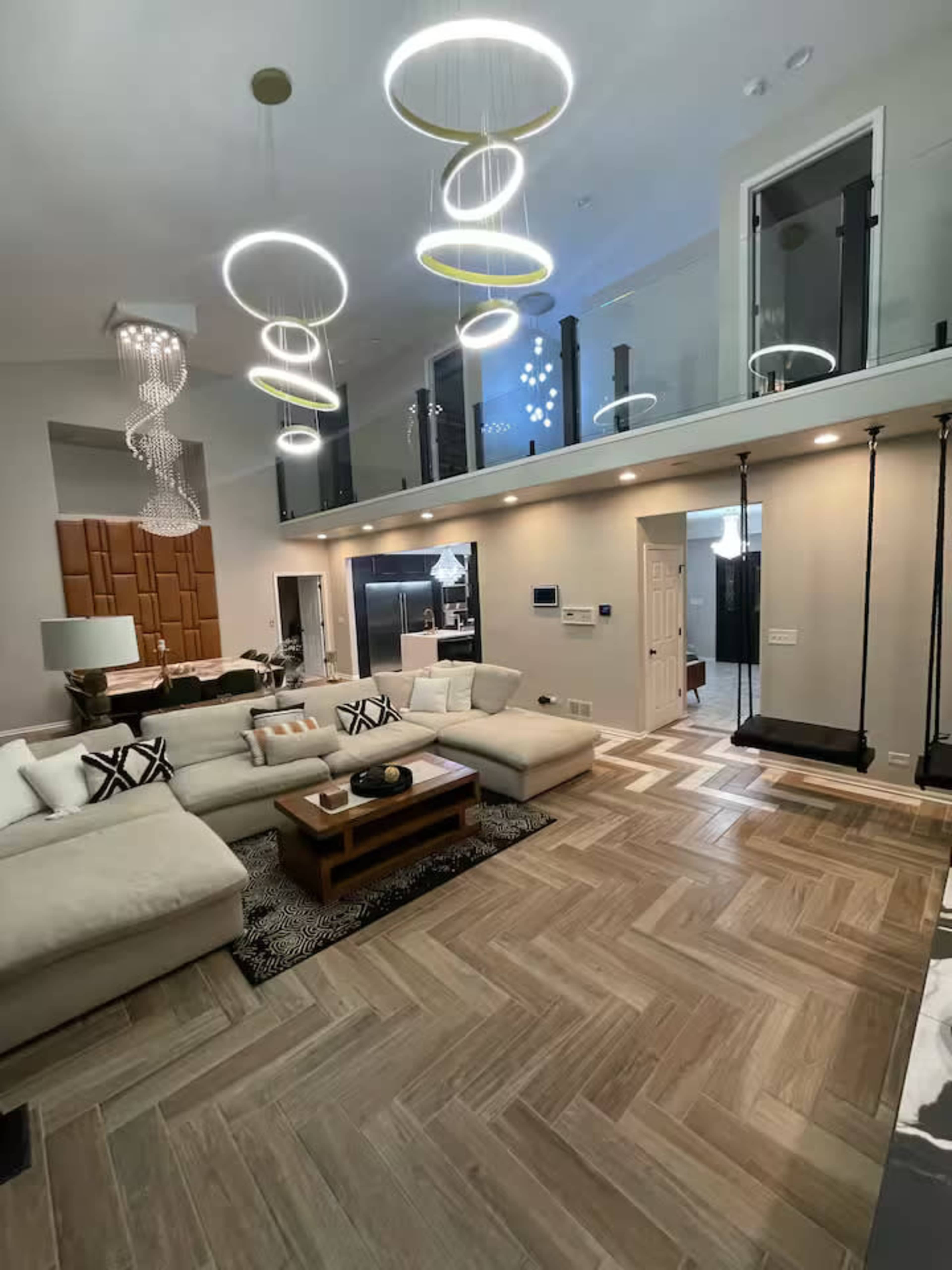 The image shows a modern living room with a large sectional sofa, a coffee table, stylish lighting fixtures, and a swing hanging from the ceiling.
