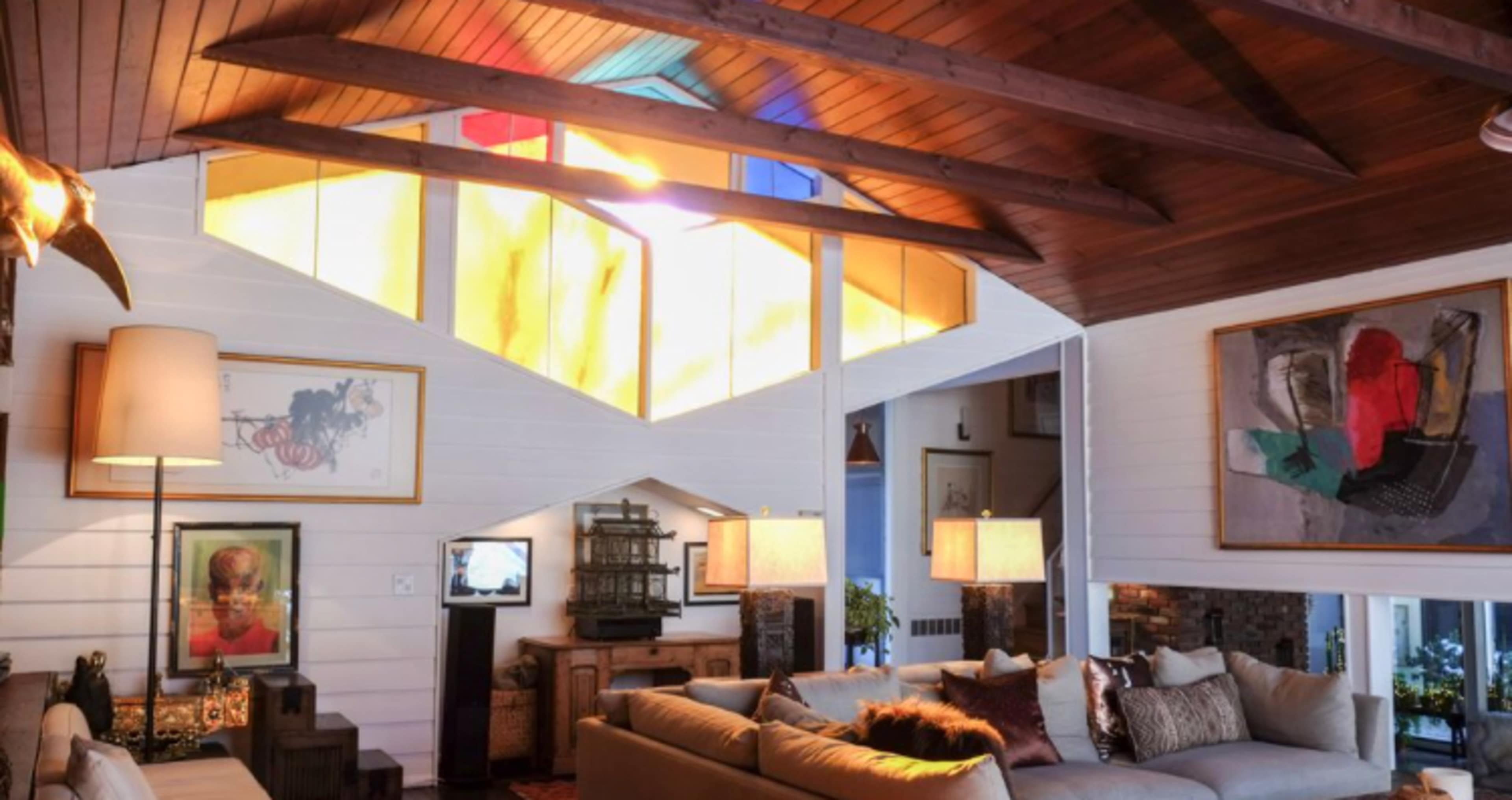 A spacious living room features a high, wooden ceiling with colorful stained glass windows and various art pieces on the walls.