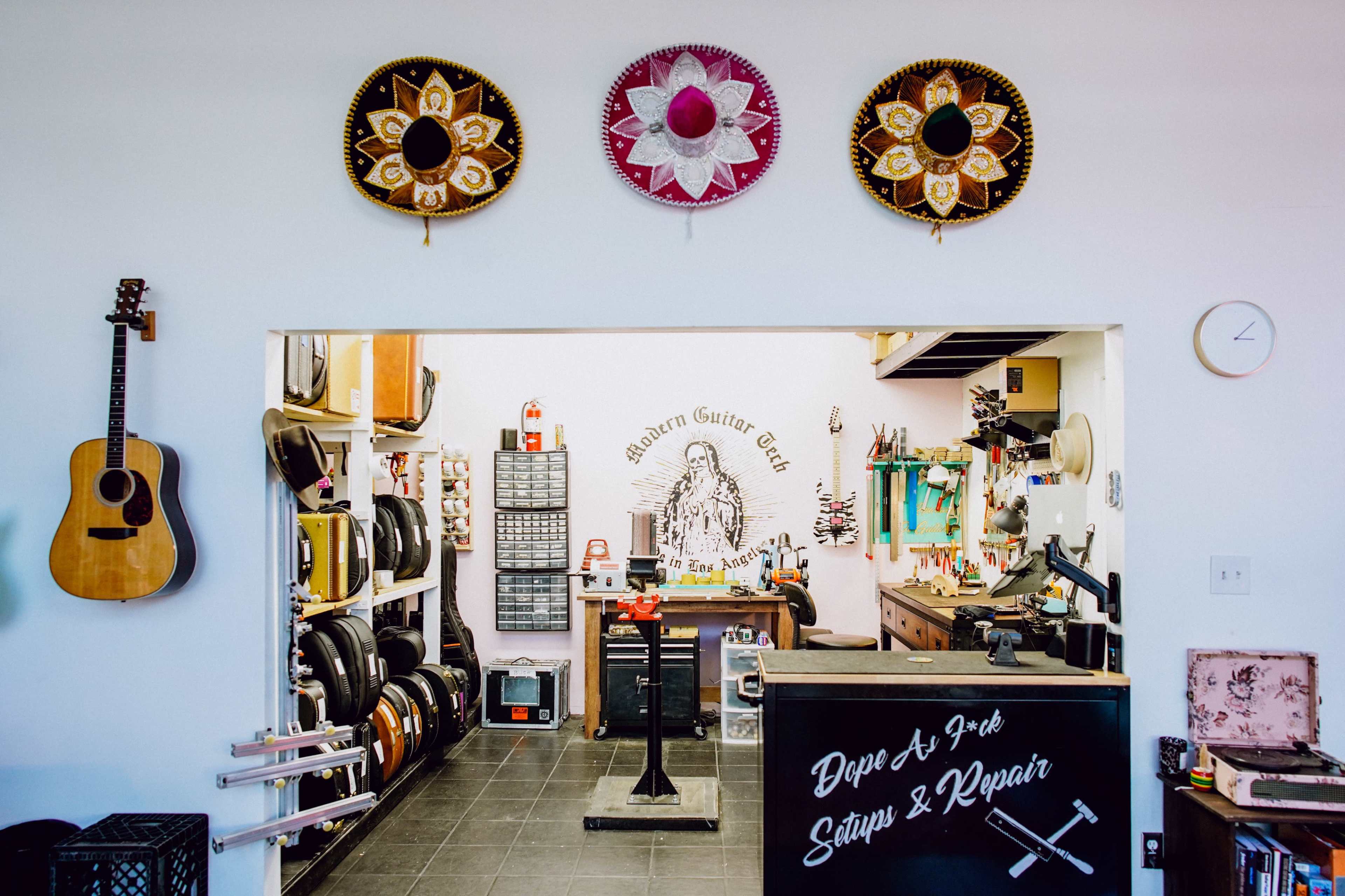 The image shows the interior of a guitar repair shop featuring an acoustic guitar, tools, and decorative sombreros on the wall.