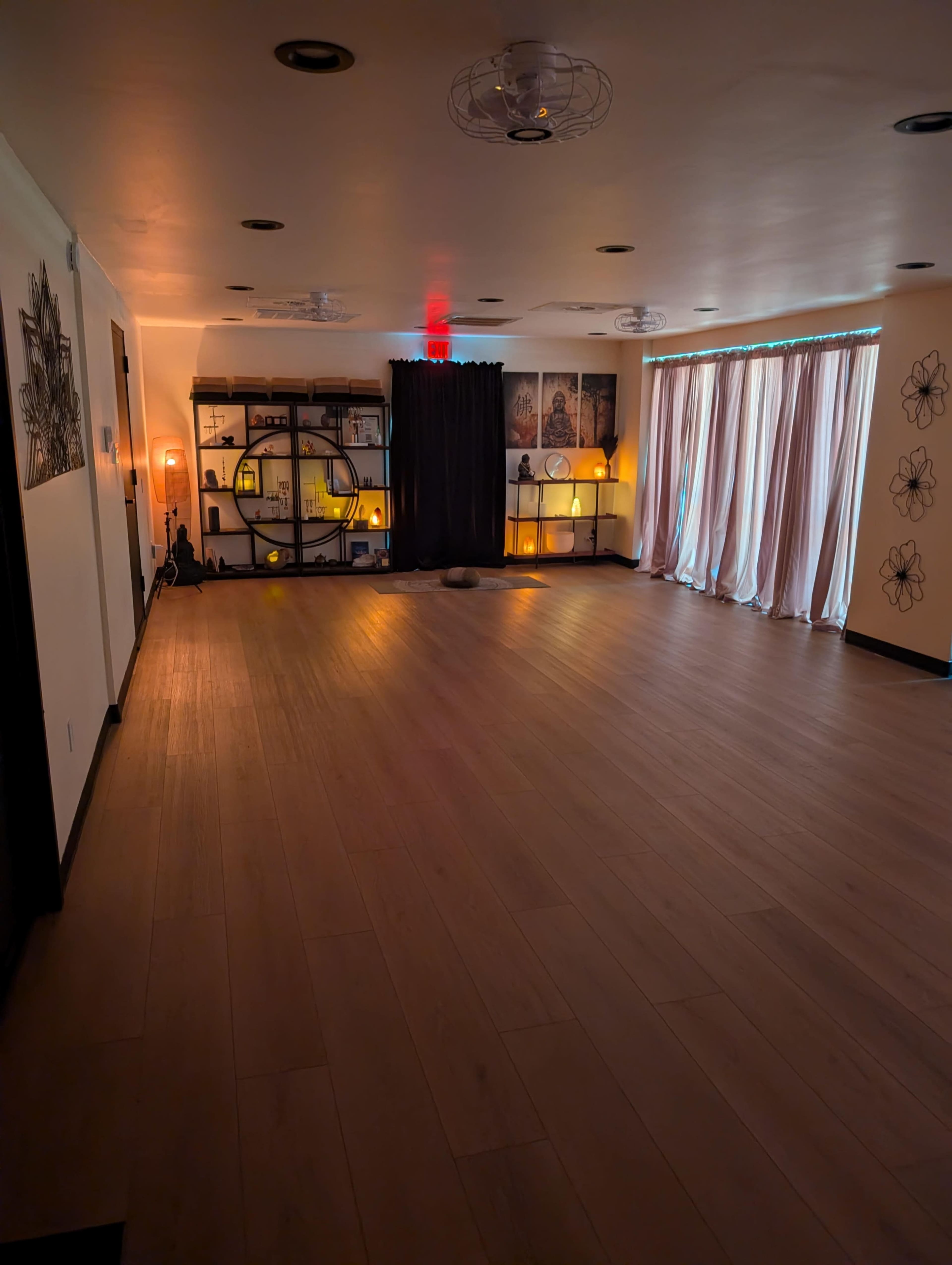 The image shows a spacious, well-lit studio with wooden flooring, shelves displaying decorative items, and soft lighting from lamps.
