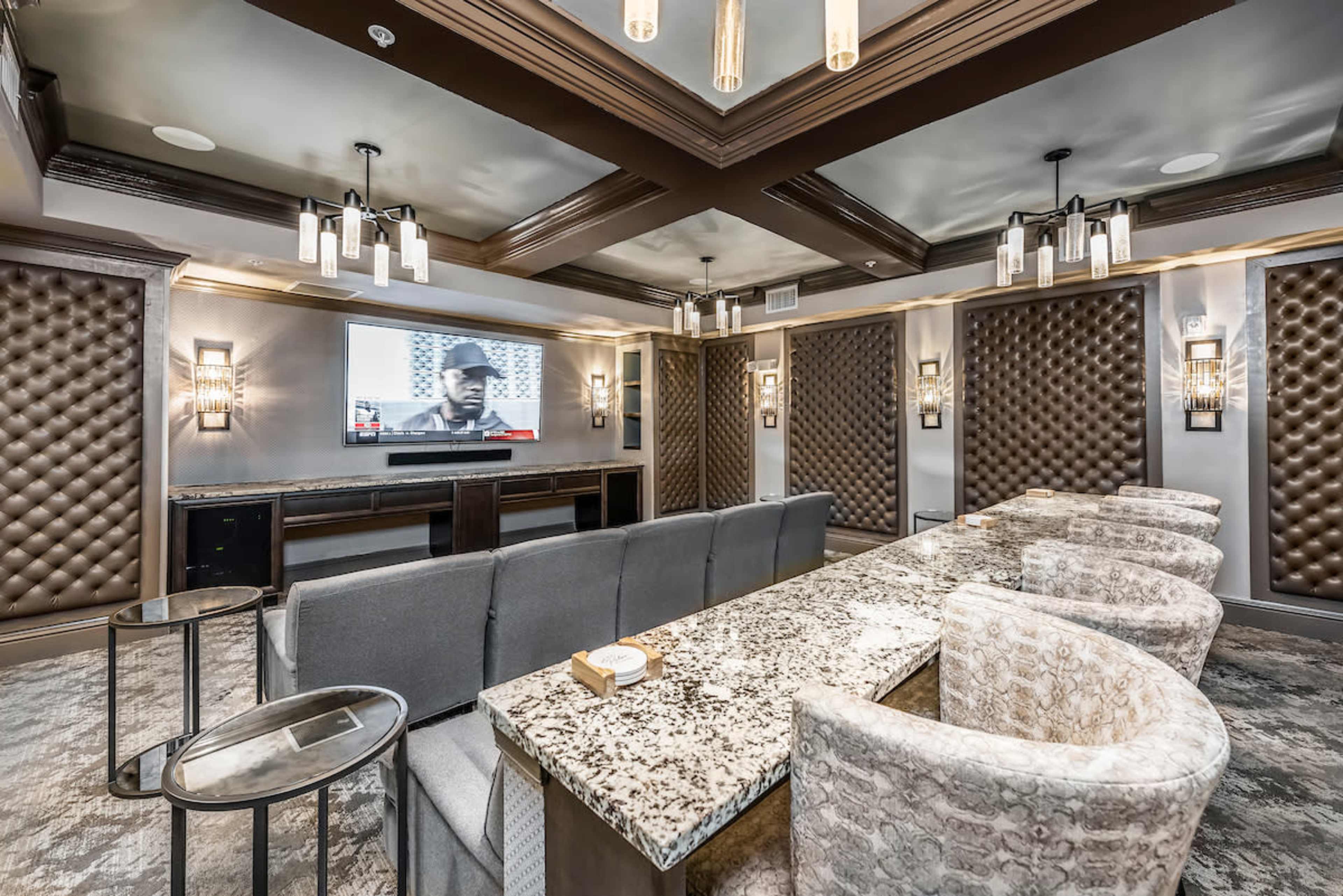 The image shows a modern room with a large table, plush seating, and a wall-mounted television featuring a black-and-white image.