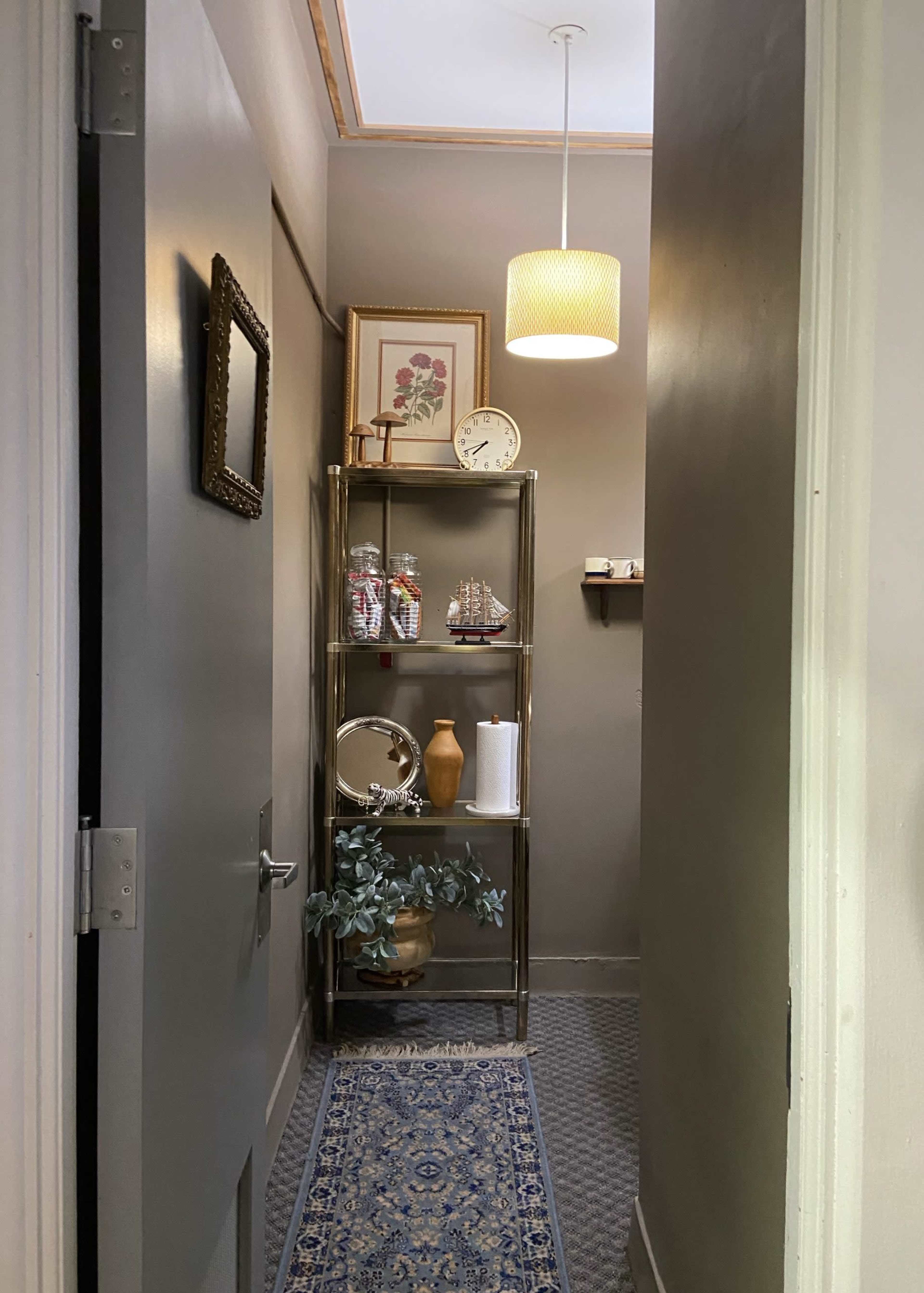 A narrow hall with gray walls, a decorative shelf featuring various items, and a pendant light hanging from the ceiling.