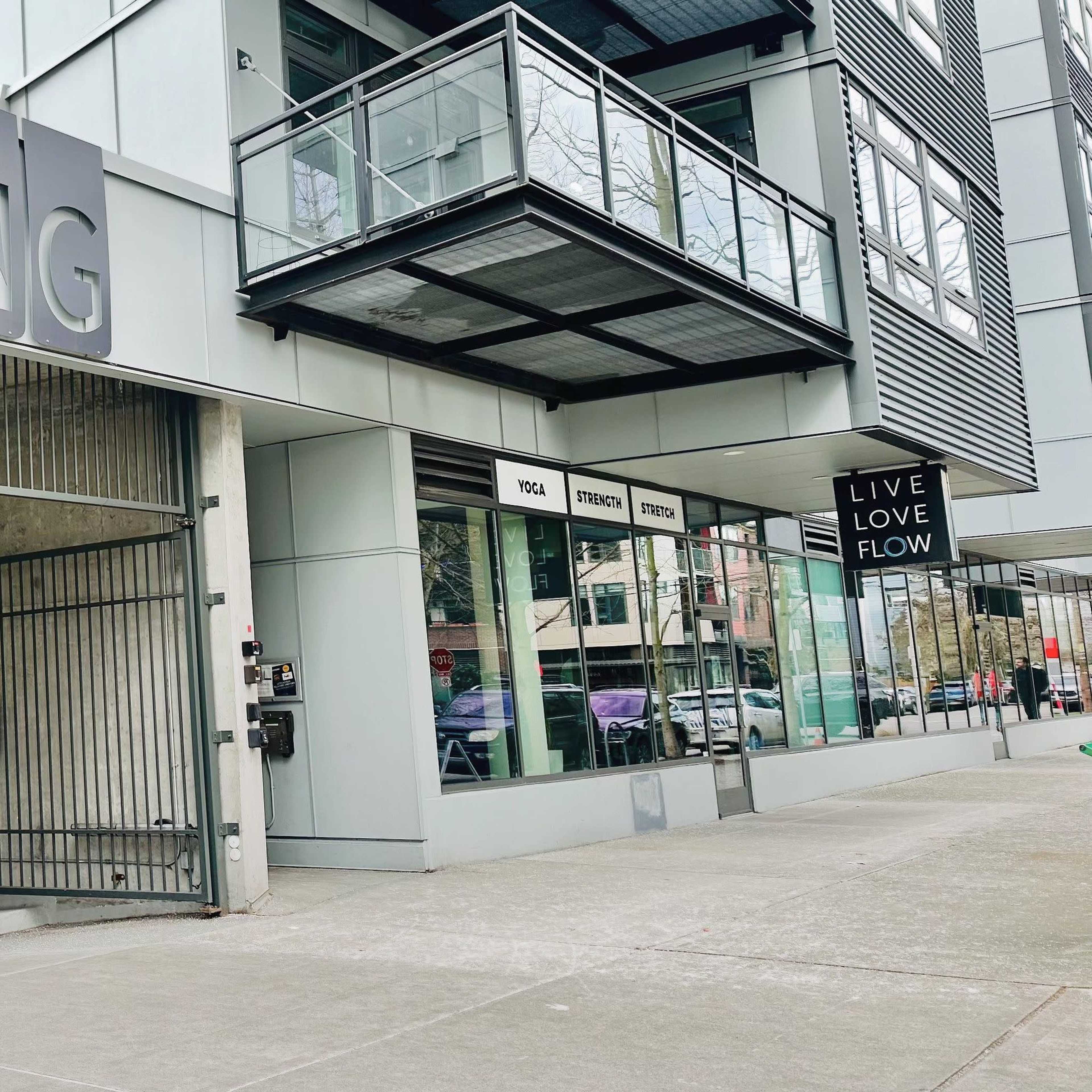 The image shows a modern building with large glass windows displaying a sign that reads "LIVE LOVE FLOW," suggesting the presence of a yoga studio.
