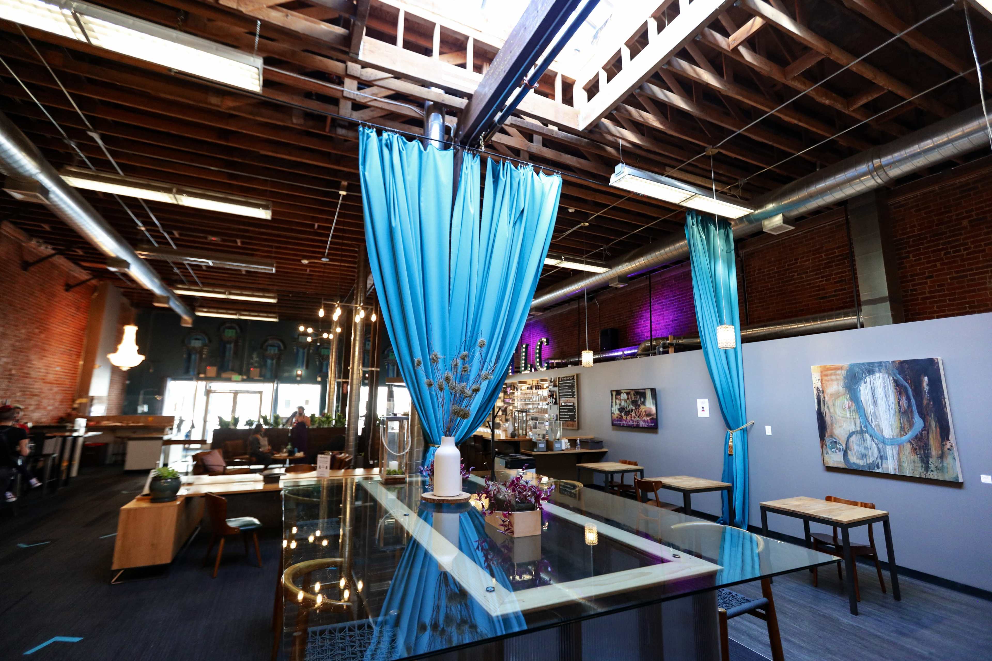 A spacious indoor area with high ceilings, featuring blue curtains, modern furnishings, and exposed brick walls.