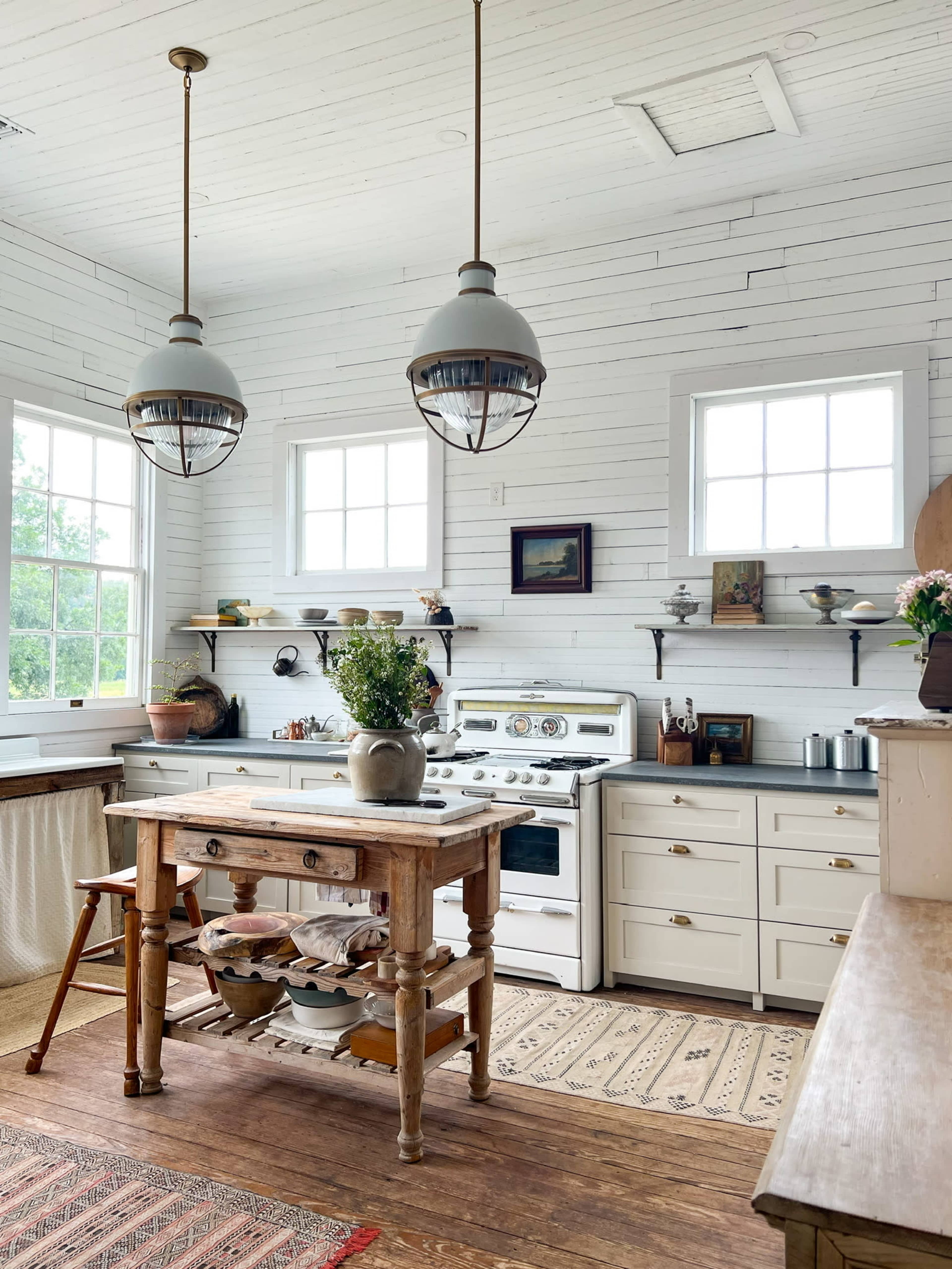A bright kitchen features white walls, wooden accents, a central table, and large windows.
