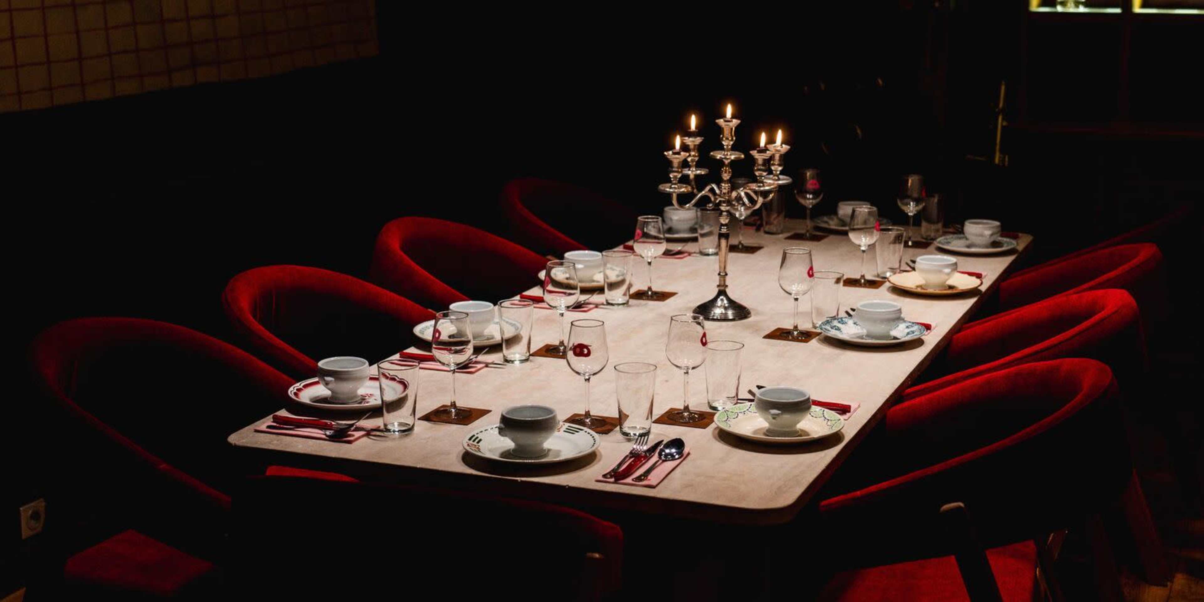 A long dining table is set with tea cups, glasses, utensils, and a candelabra in a dimly lit room.