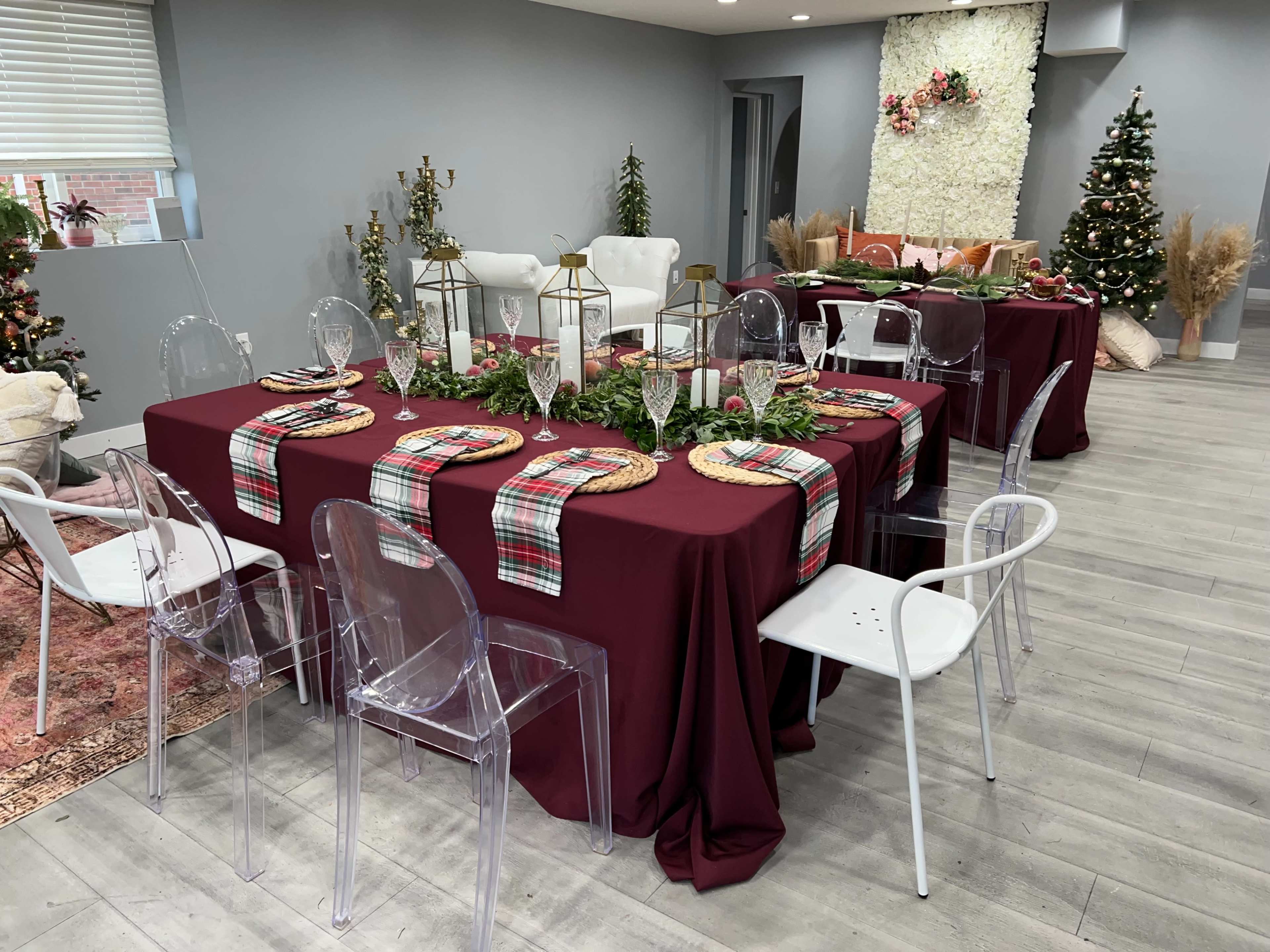 A dining area is arranged with burgundy tables, clear chairs, and festive decorations, including holiday-themed table settings and trees.