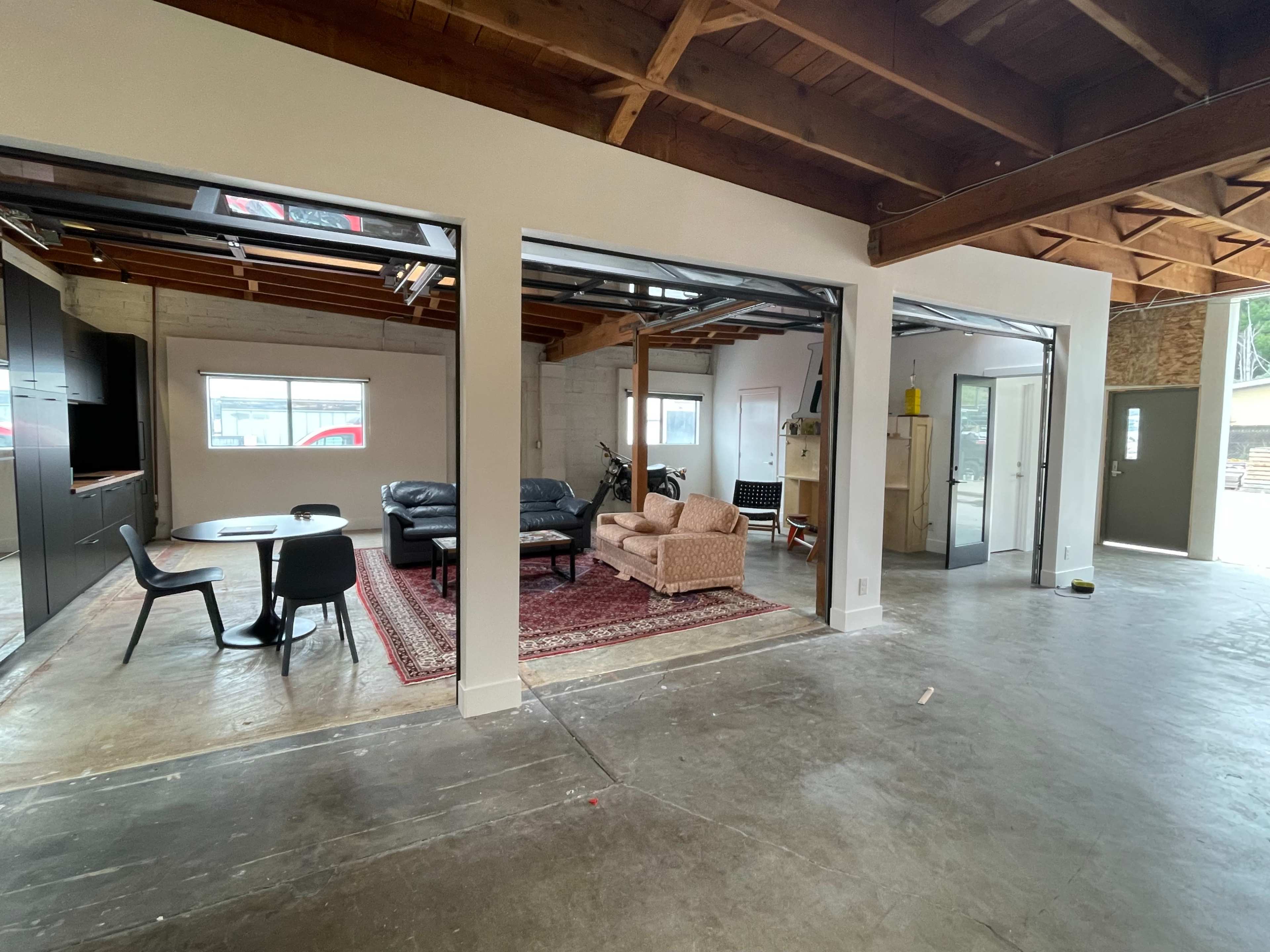 An open-concept living space with a dining area on the left and a sitting area on the right, featuring exposed beams and a concrete floor.