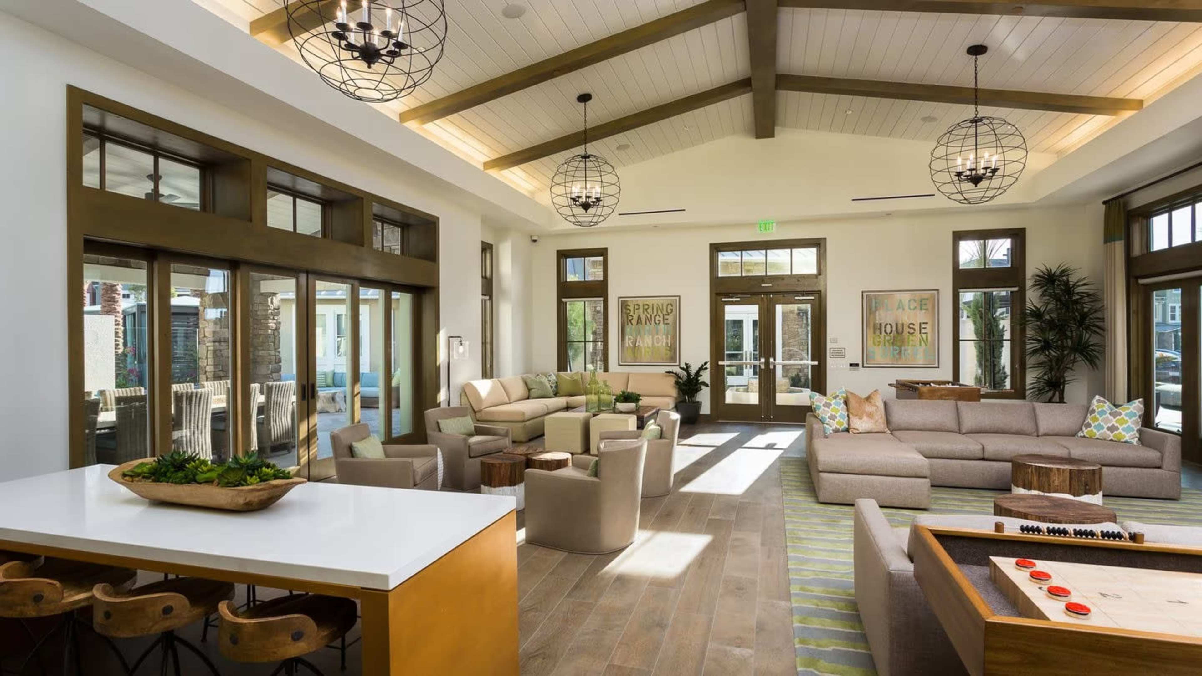 A spacious, well-lit lounge area featuring a modern seating arrangement, large windows, and rustic wooden beams overhead.