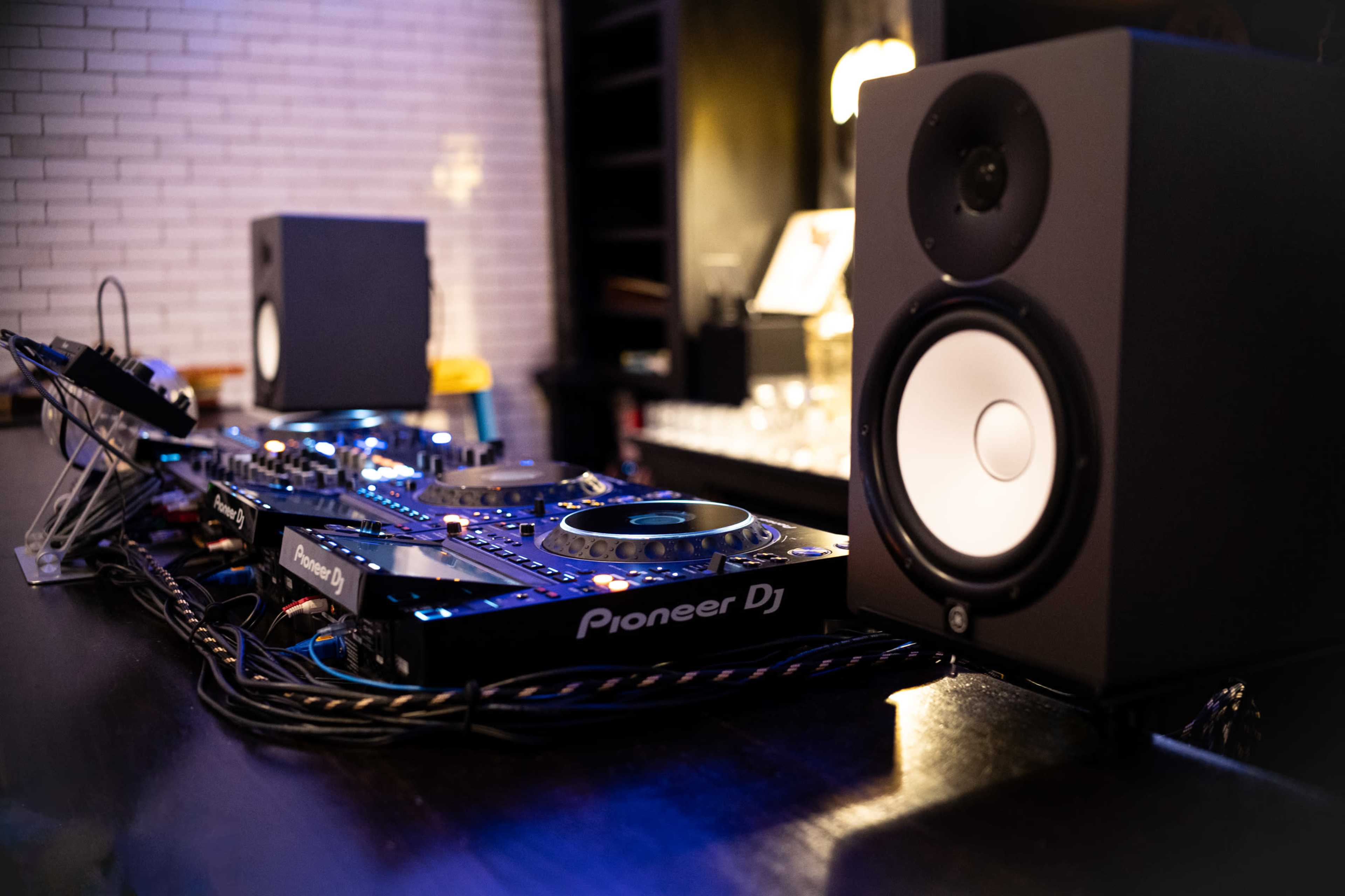 A DJ setup featuring Pioneer equipment, including a mixer and turntables, is placed next to black studio speakers on a bar counter.