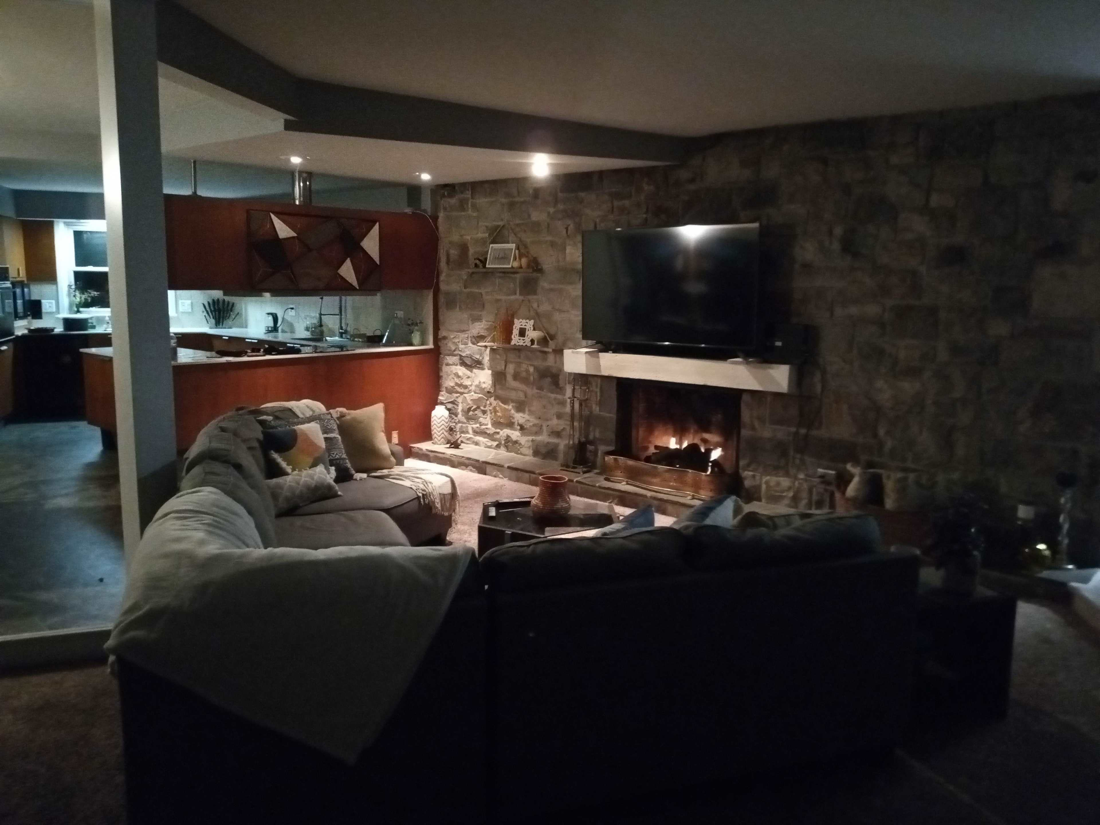 A living room with a stone wall, a fireplace, and a large television mounted above a mantel, surrounded by a sectional couch.