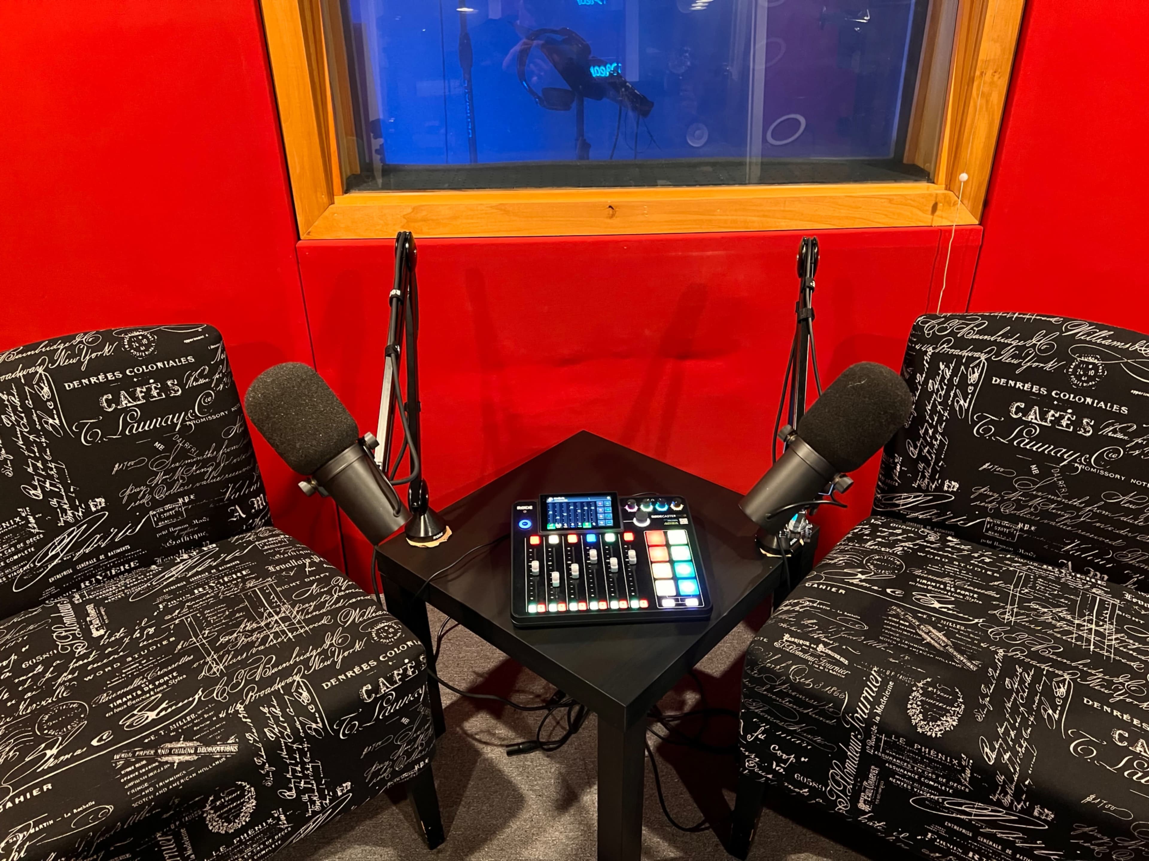 The image shows a recording studio setup with two chairs and a mixer with microphones positioned on a table between them.