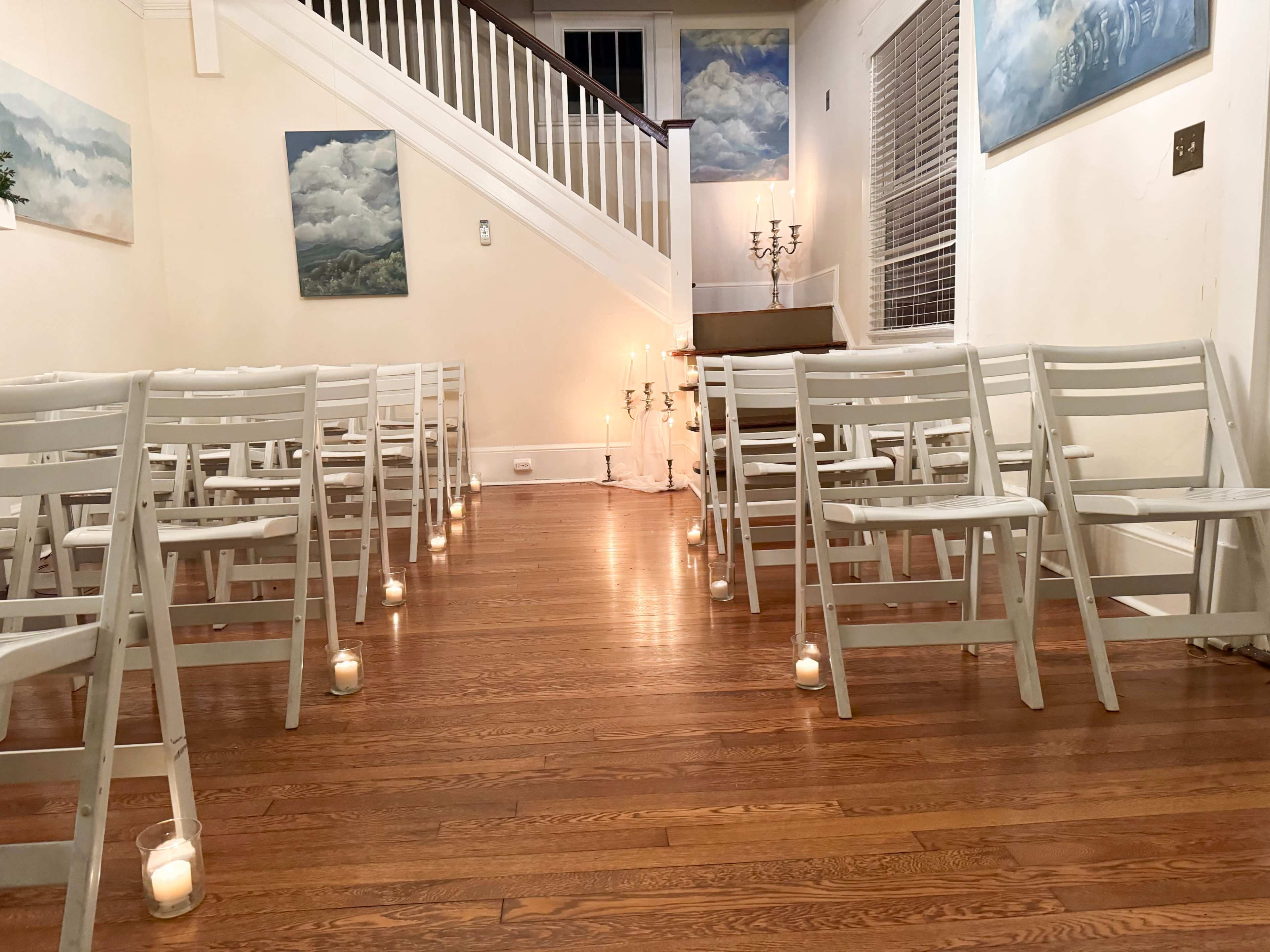 A small indoor venue with white folding chairs arranged in rows and candles illuminating the space along a wooden floor.