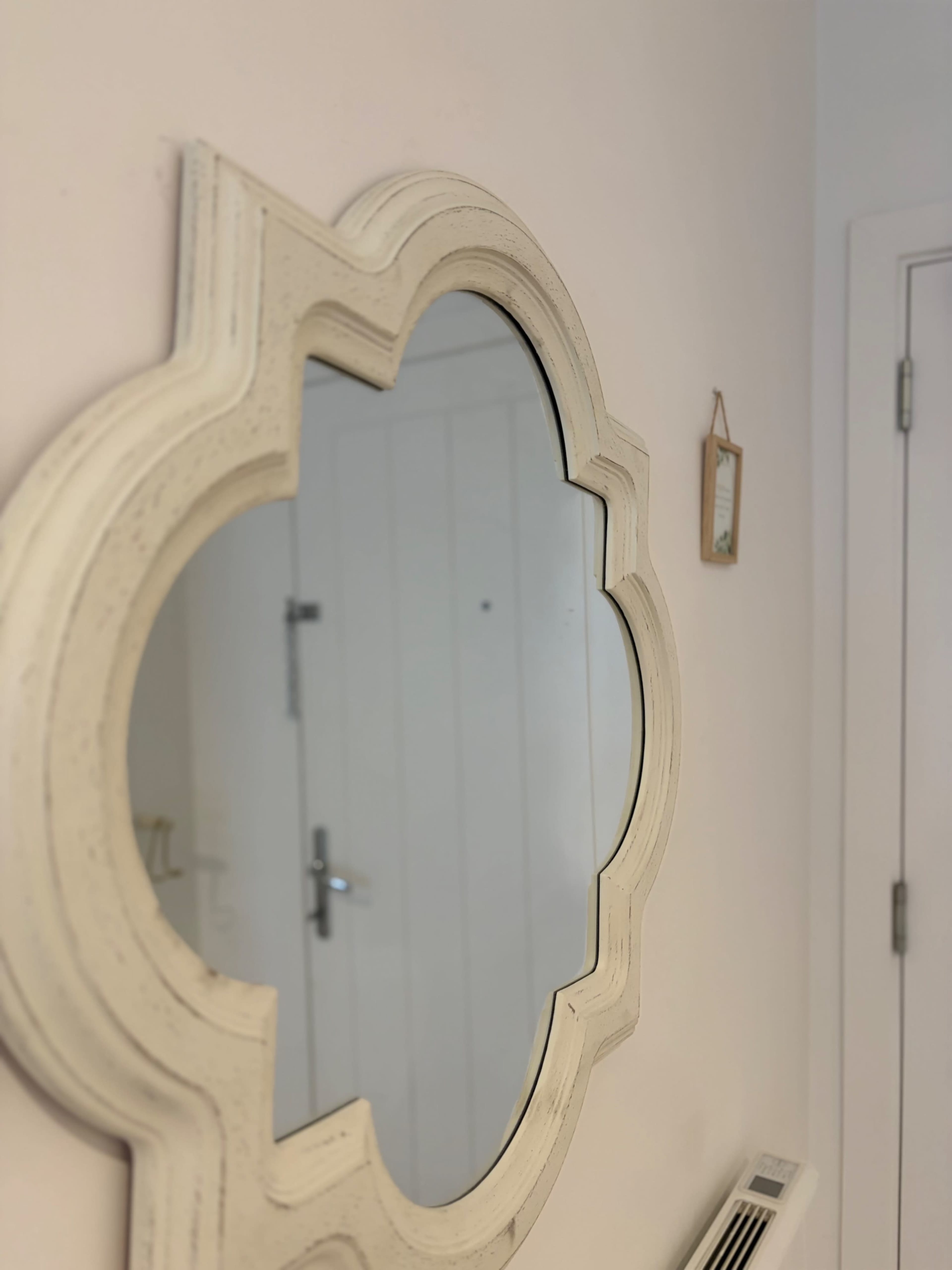 A decorative mirror with a scalloped edge is mounted on a light-colored wall near a door.