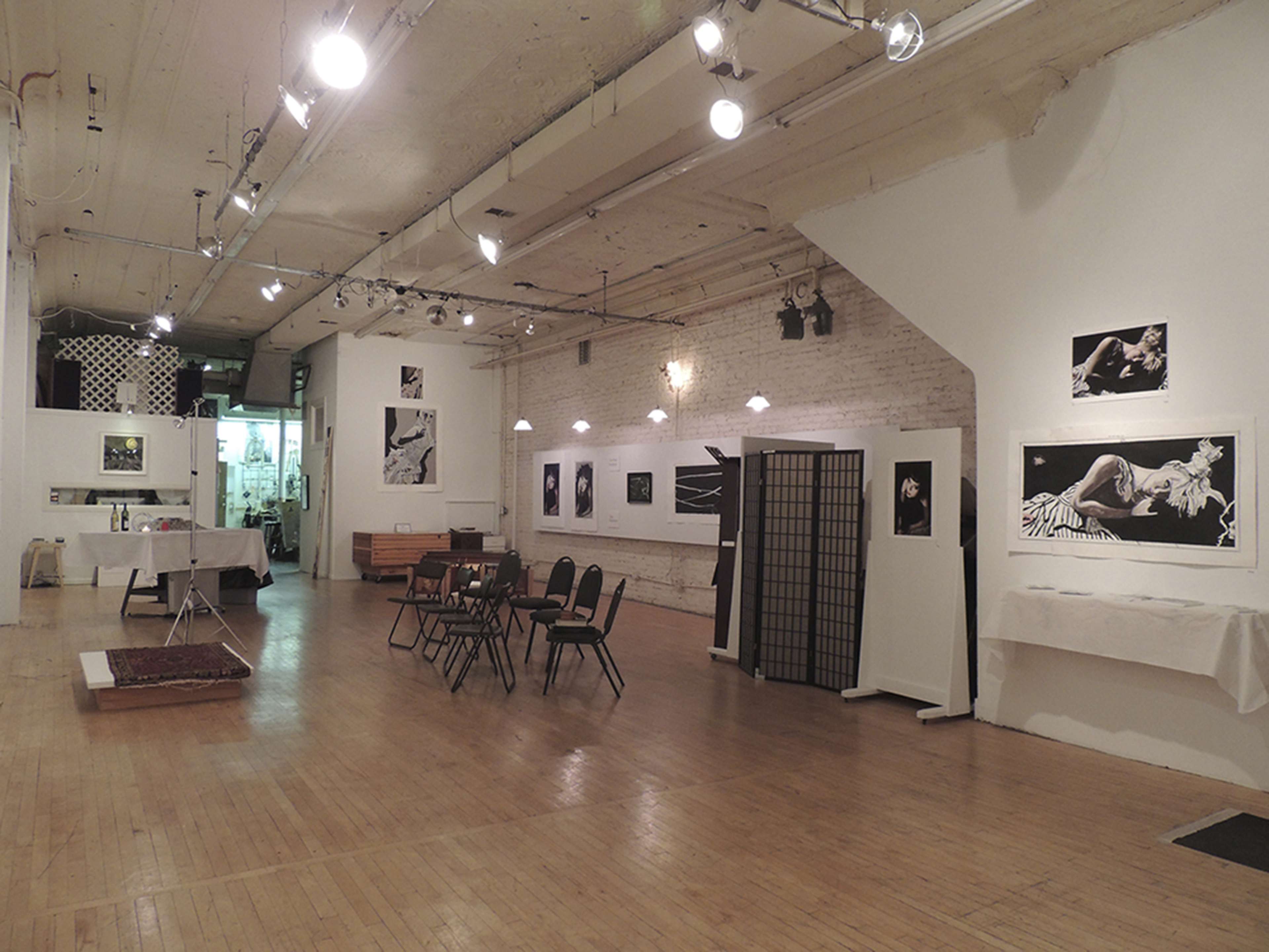 An art gallery featuring black and white photographs displayed on the walls, with a seating area in the center and wooden flooring.