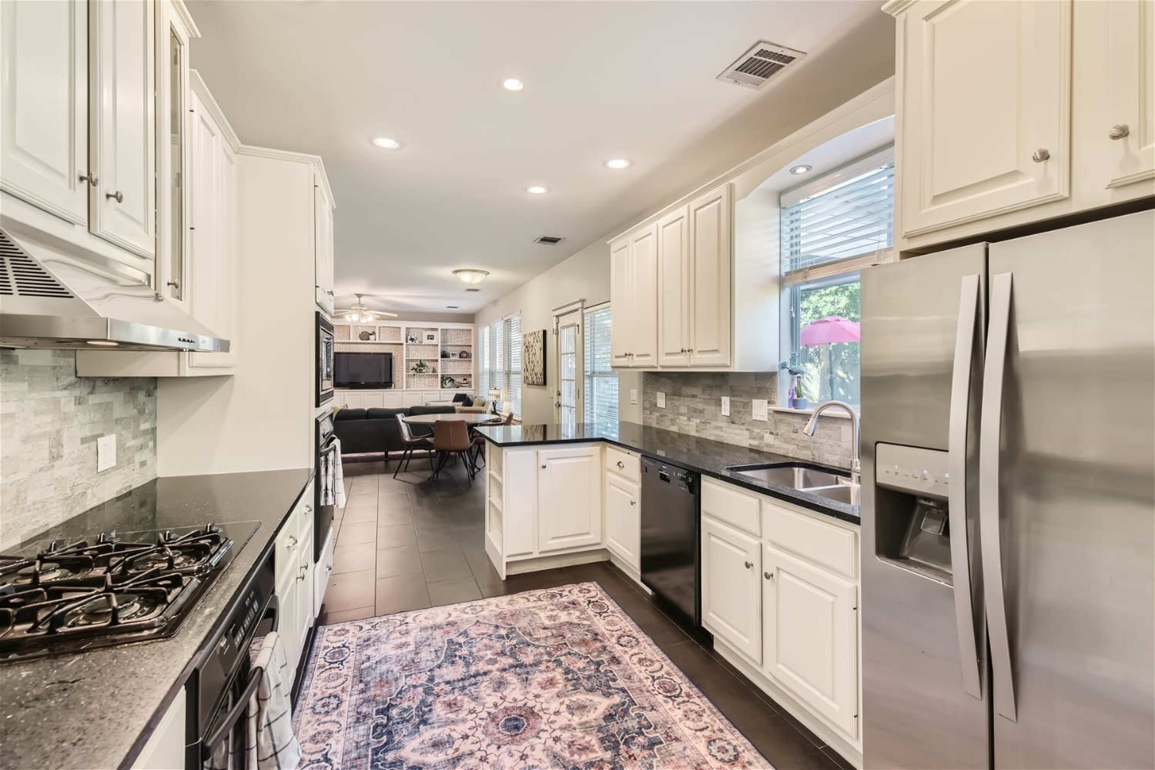 A modern kitchen with white cabinets, stainless steel appliances, and a tiled floor, leading into an open living area.