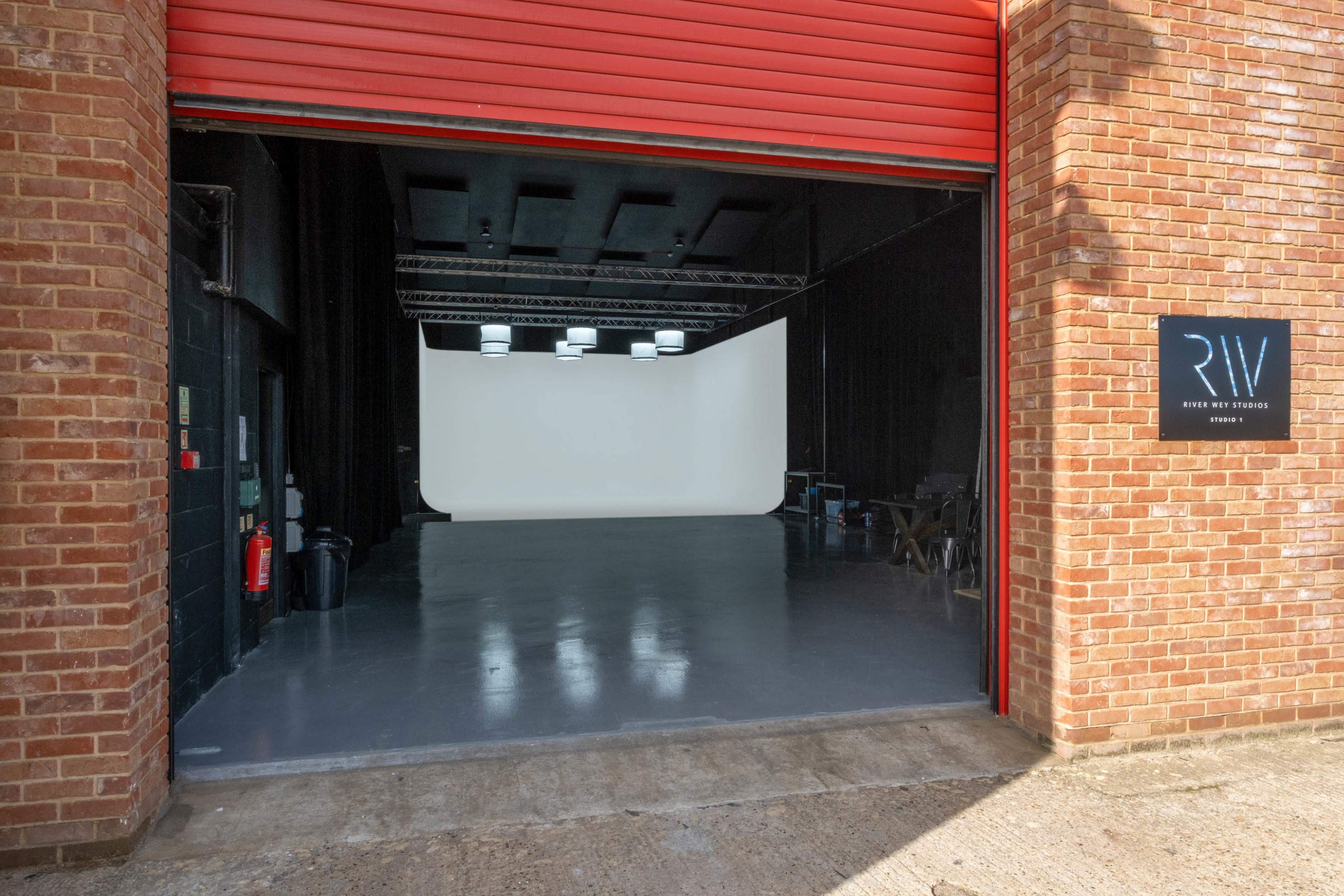 A red garage door opens to a clean, empty studio space with a white backdrop and overhead lighting.
