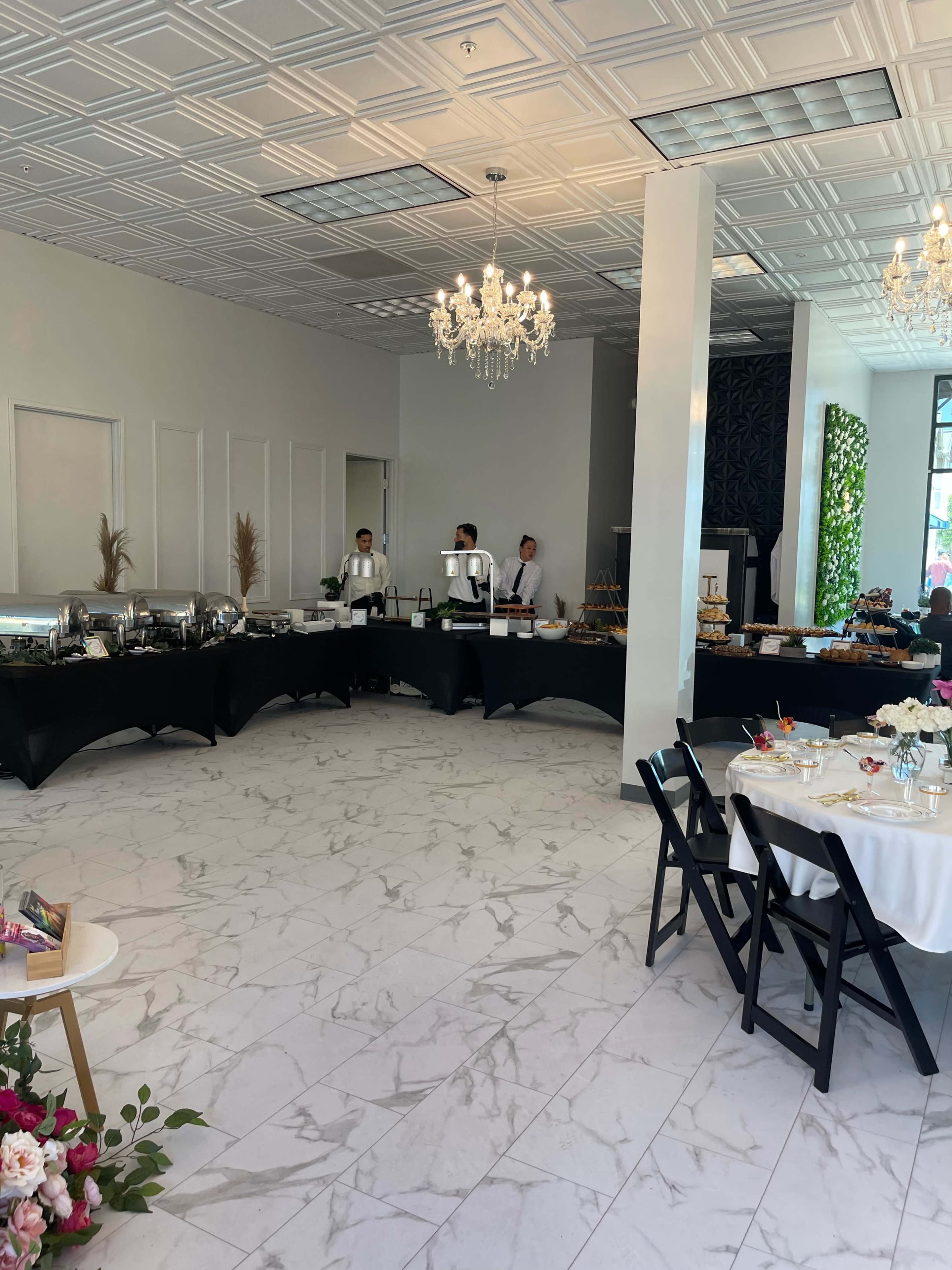 A spacious event area with a buffet table, two servers, and round tables set for dining.