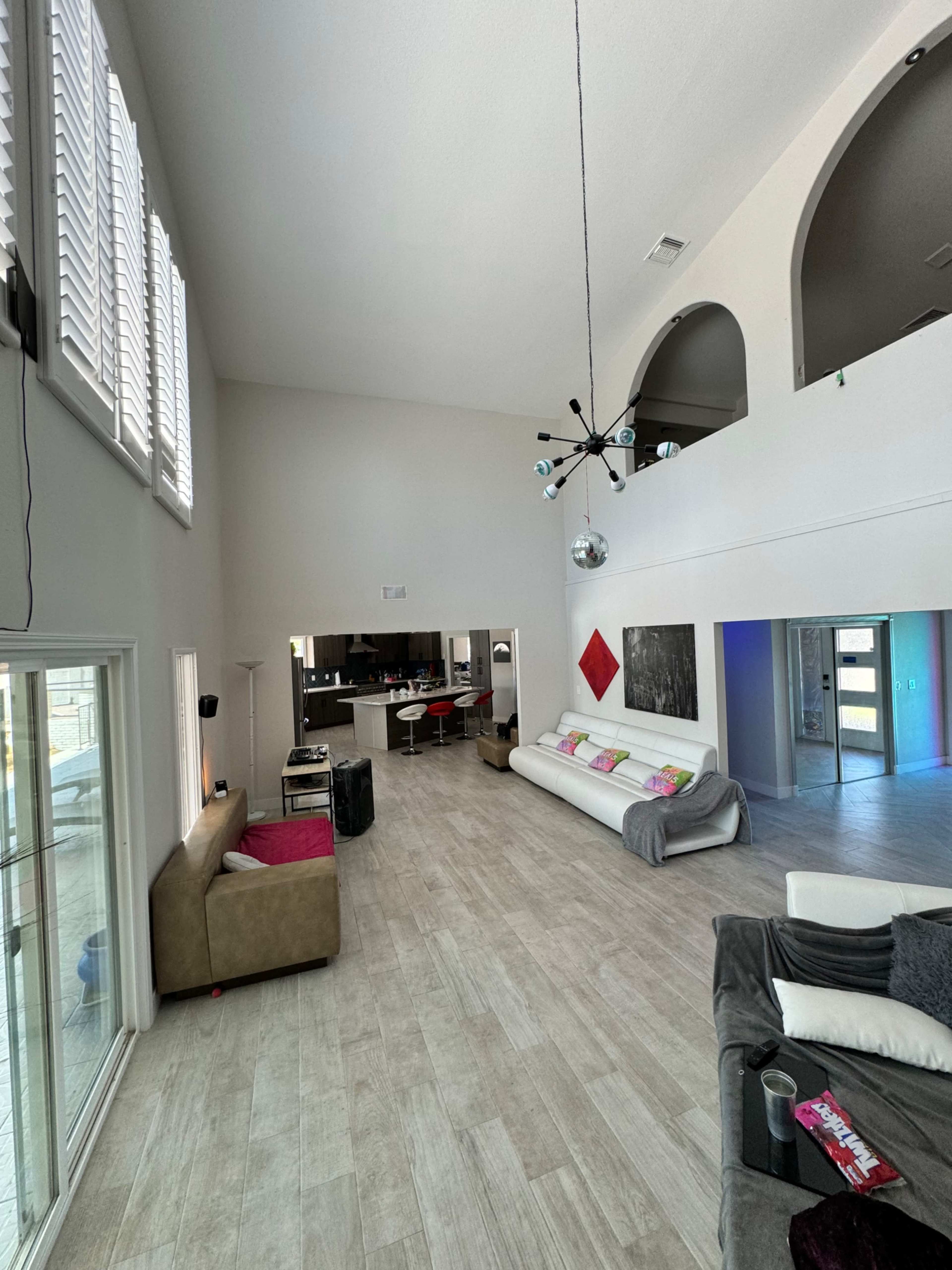 A spacious living area with high ceilings, modern furniture, and an open layout leading to a kitchen and dining area.