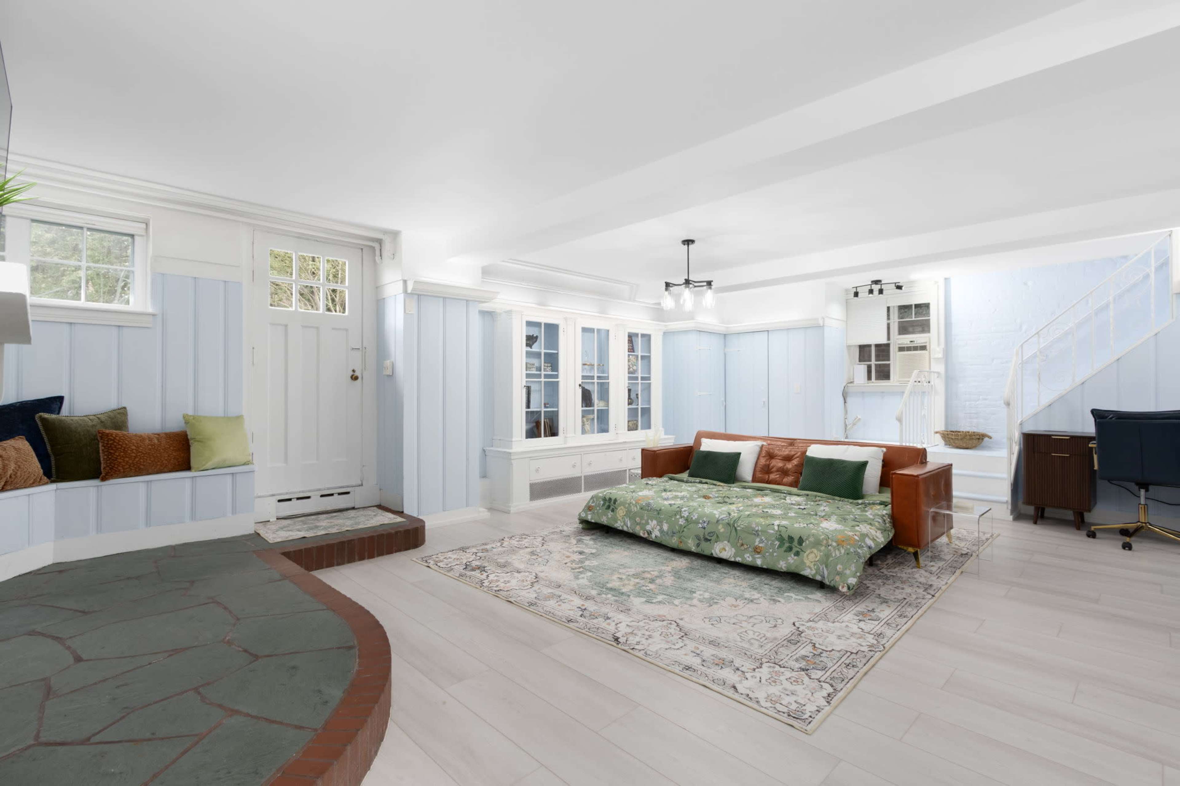The image shows a spacious, light-colored basement featuring a seating area with a floral-patterned sofa and a small seating nook by the entrance.
