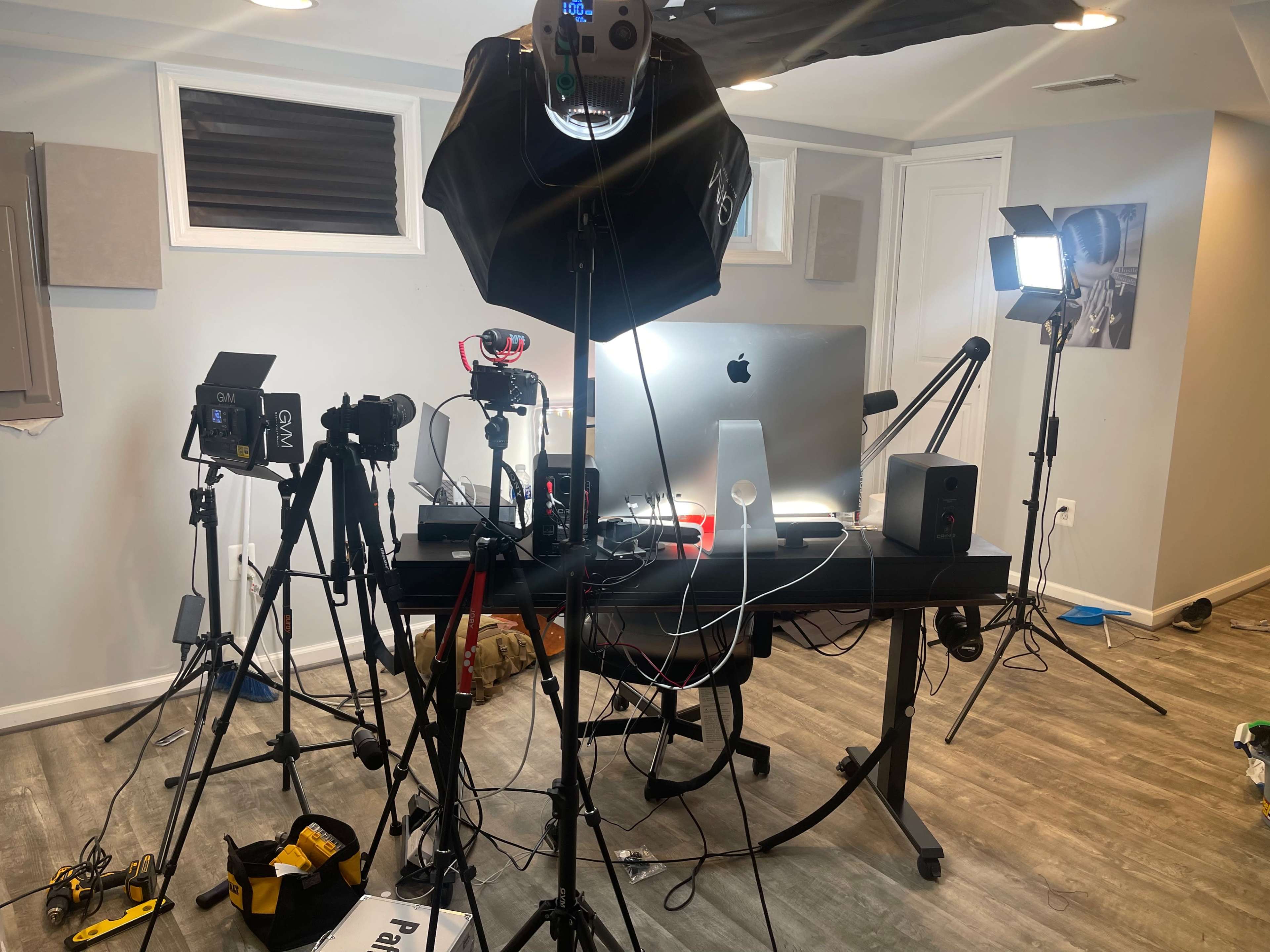 A photography and video setup is arranged in a room, featuring cameras, lighting equipment, and a computer on a desk.