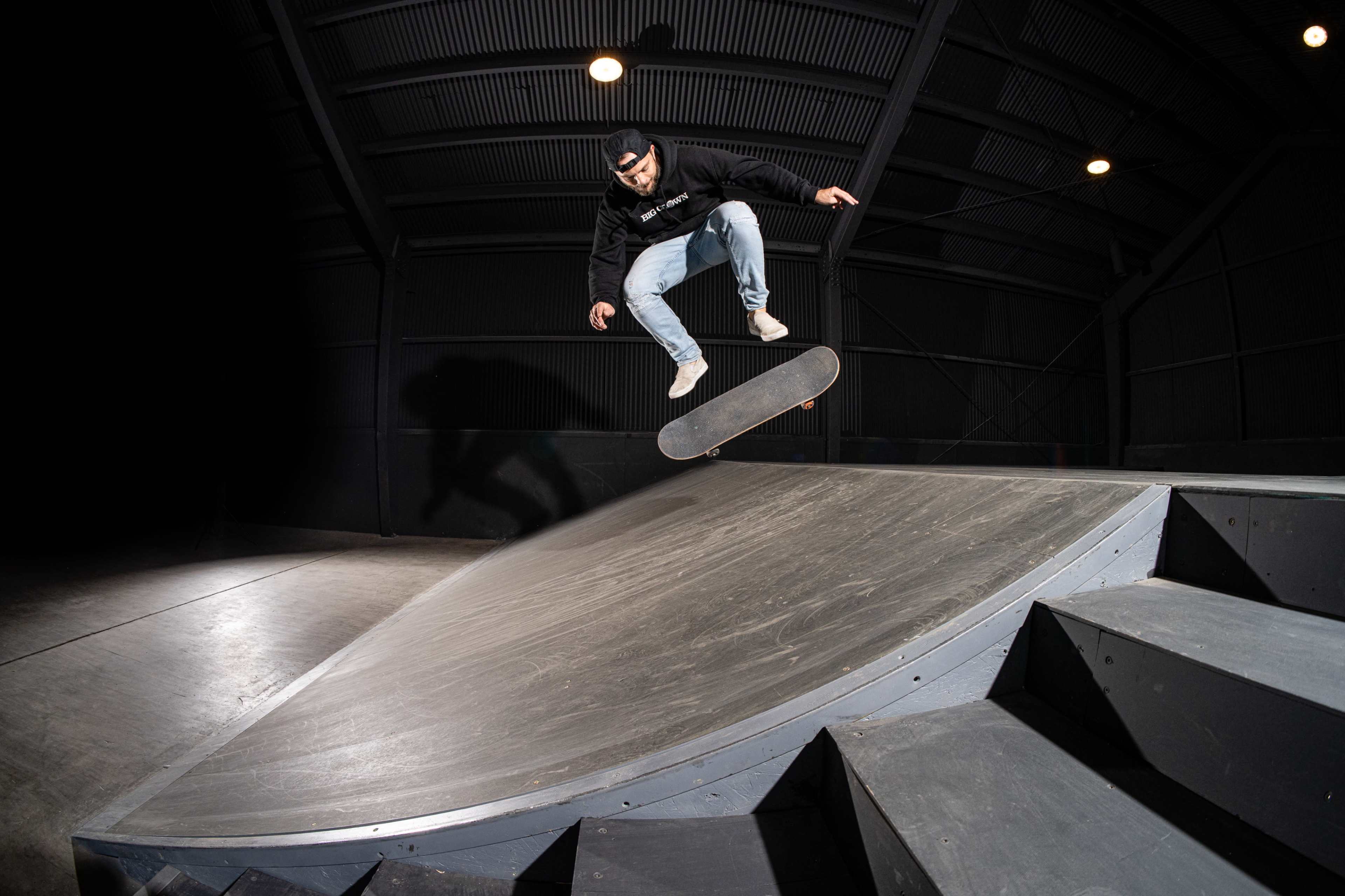 A skateboarder performs a jump on a ramp inside a dimly lit skatepark.