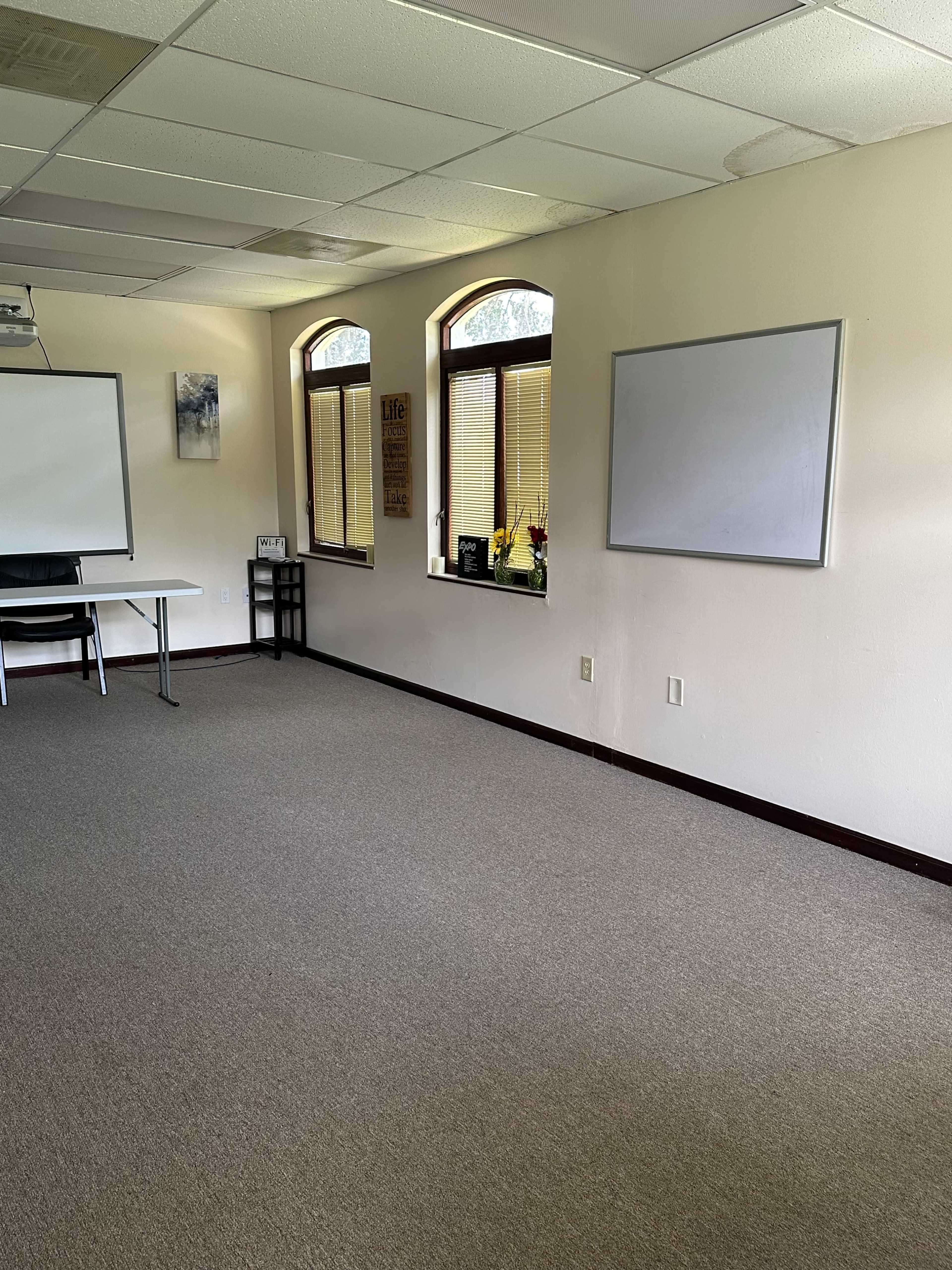 A sparsely furnished meeting room with a table, chairs, and two windows.
