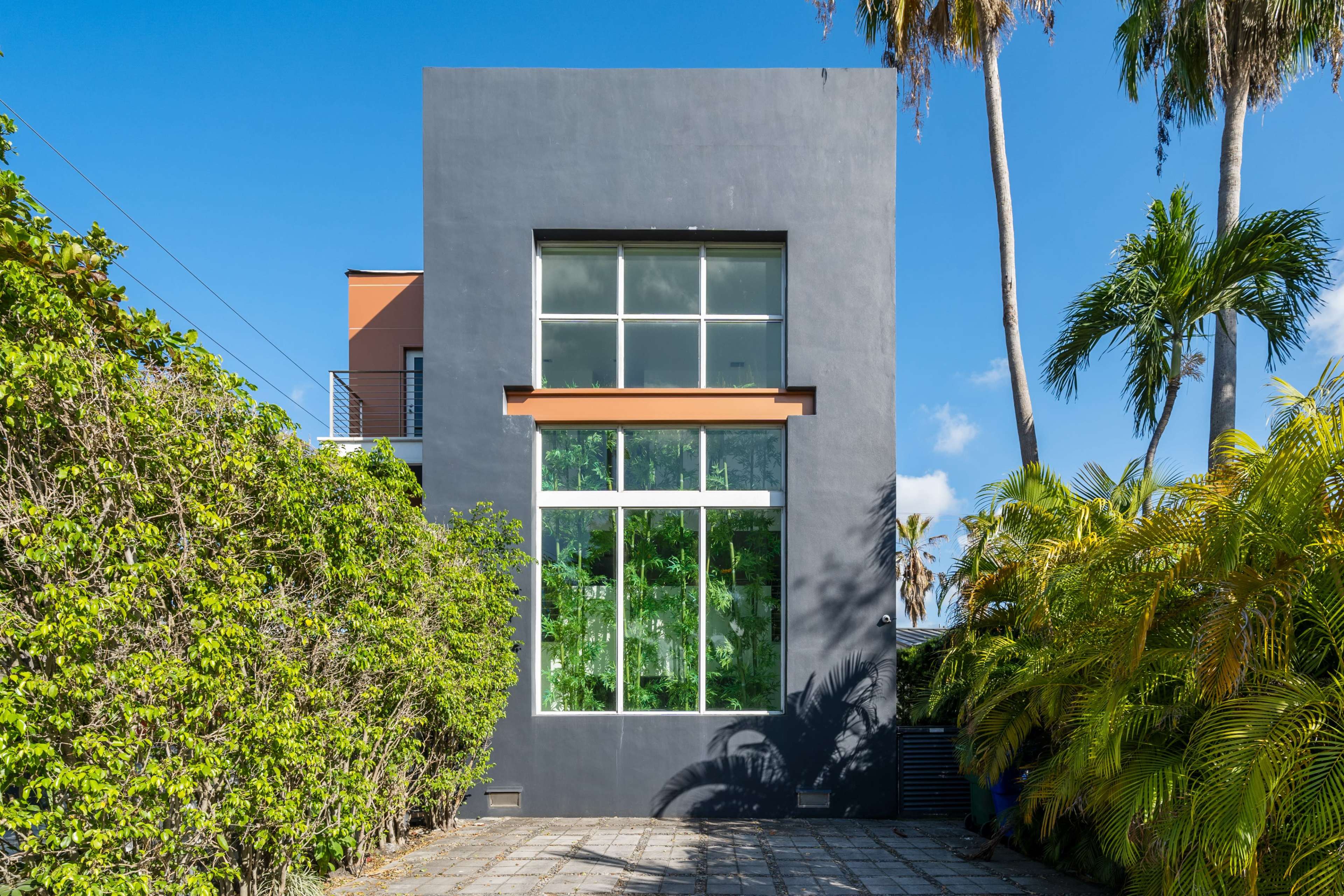 A modern, gray building with large windows surrounded by lush greenery and palm trees under a clear blue sky.