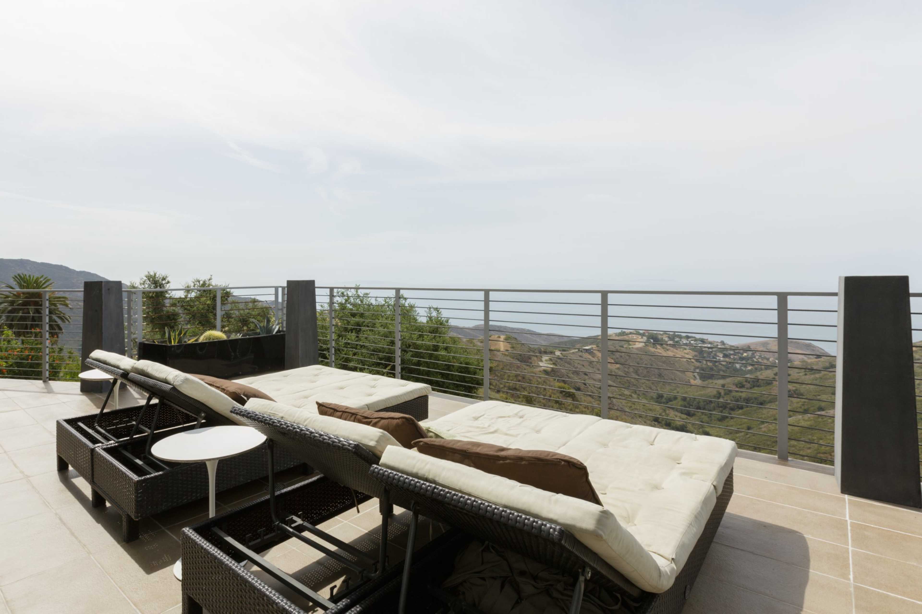 Two lounge chairs on a terrace overlooking a hilly landscape and the ocean in the distance.