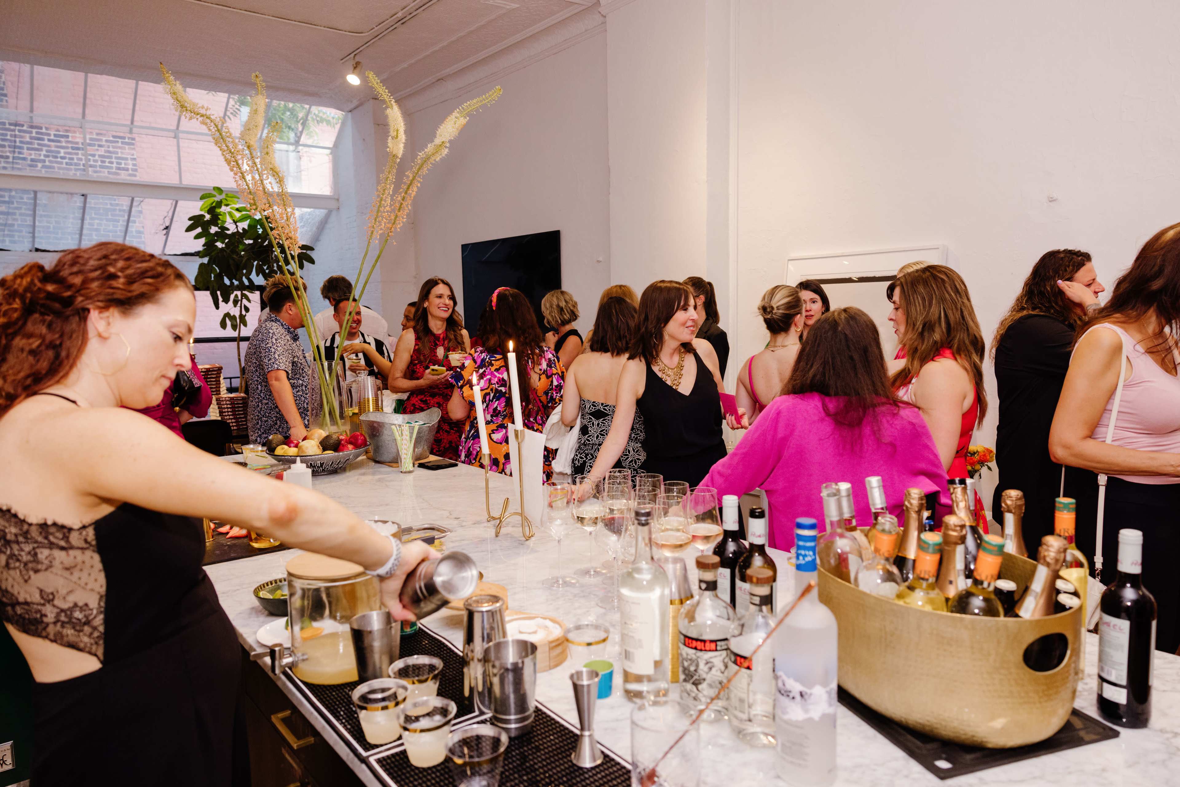 A crowd of people socializes at a lively gathering with a bar area serving various drinks.