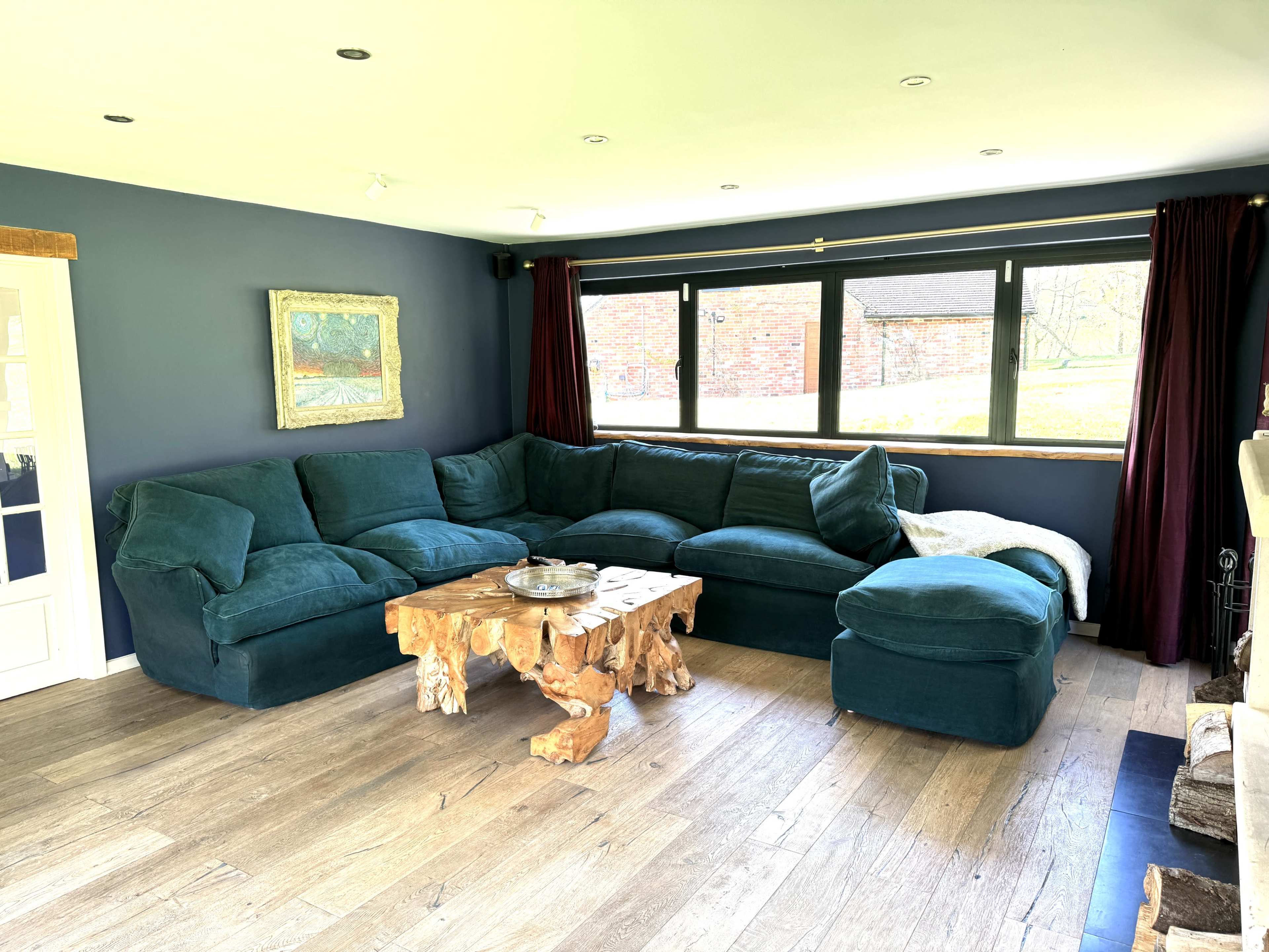 A living room with a large dark green sectional couch and a unique wooden coffee table, complemented by a window that offers a view of the outdoors.