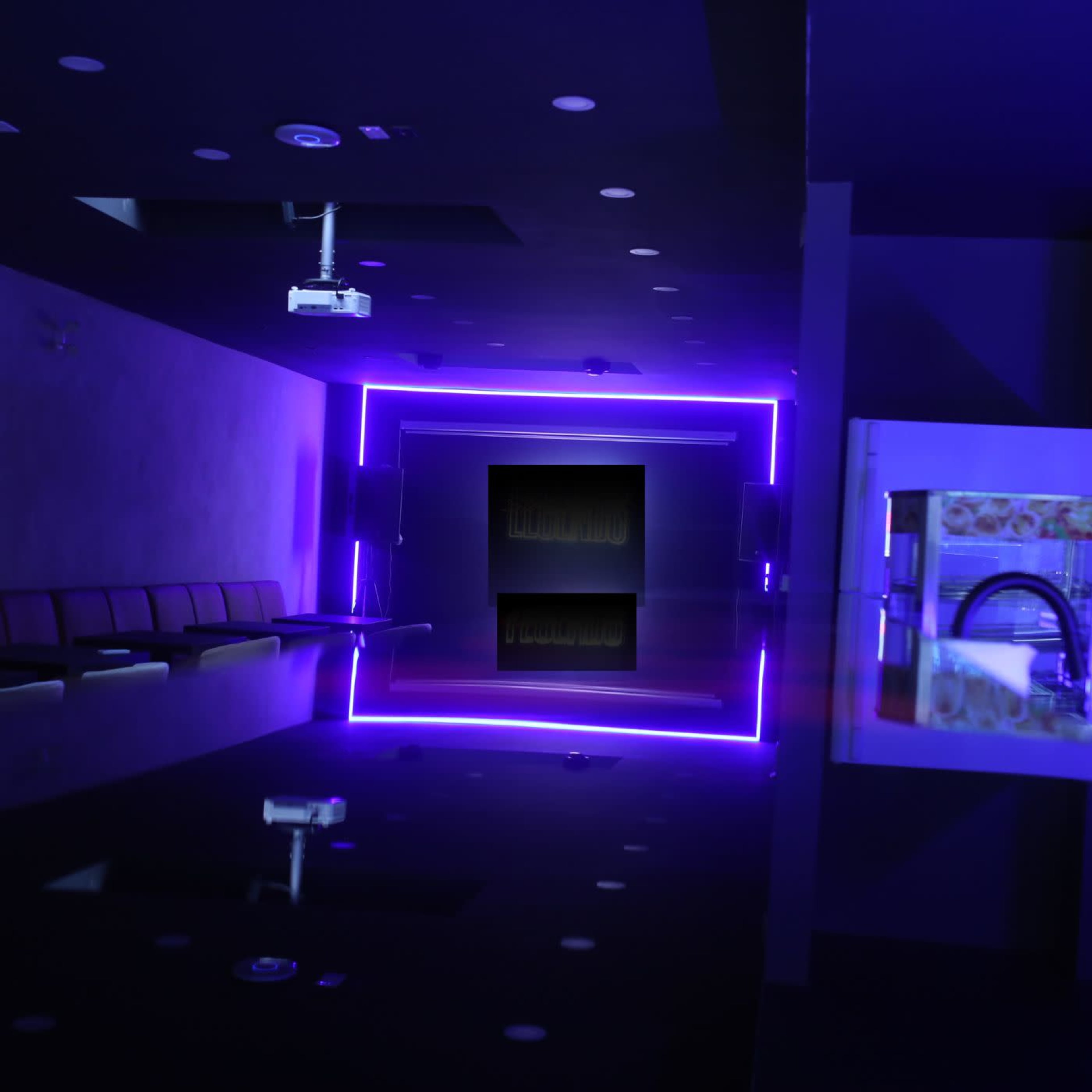 The image shows a dimly lit bar area with purple neon lighting and a reflective surface, featuring a projection screen at the far end.
