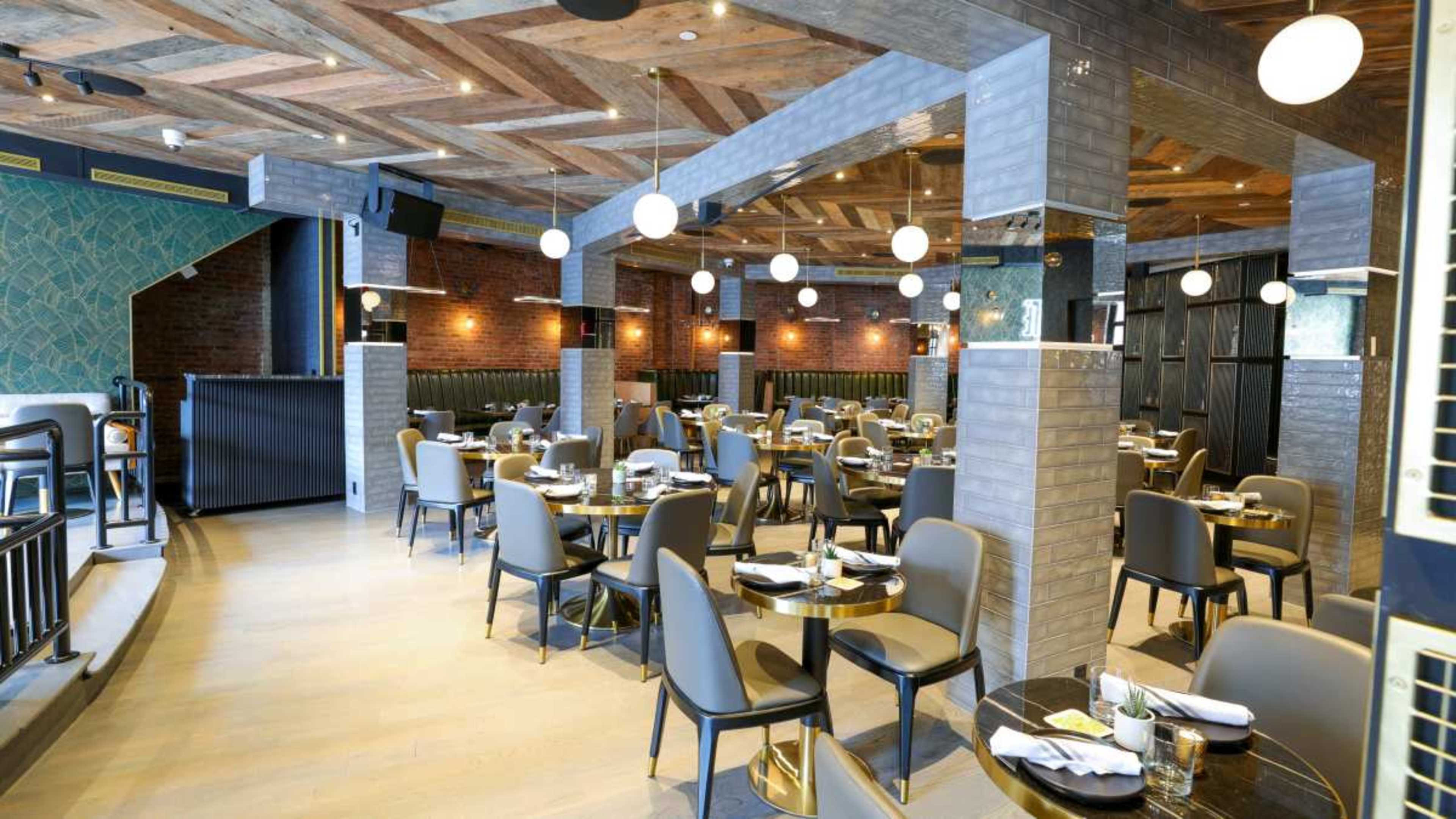 The image shows a modern restaurant interior with wooden beams, circular light fixtures, and neatly arranged tables and chairs.