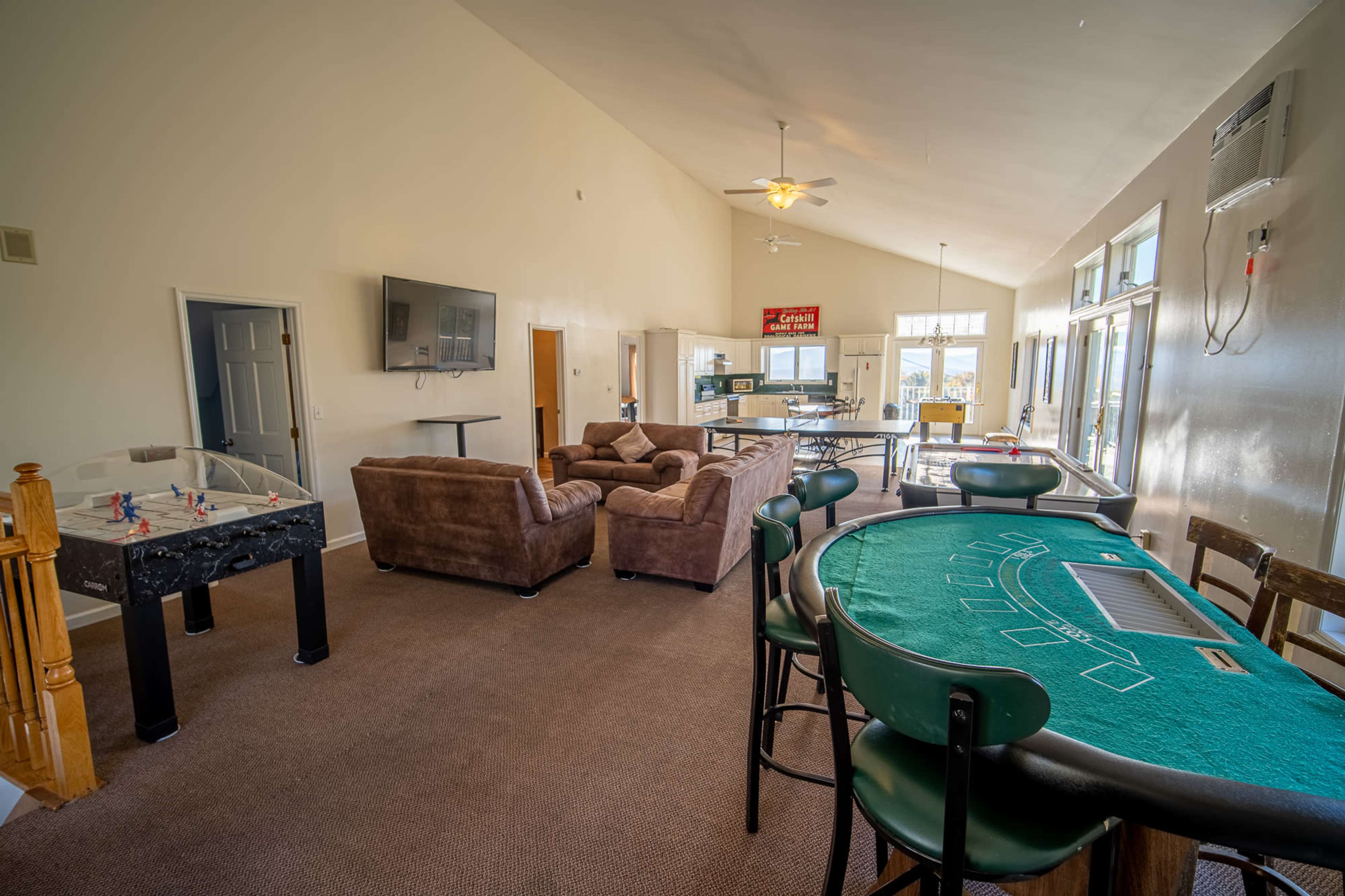 The room features a casual gathering space with a poker table, a foosball table, comfortable seating, and a large television.